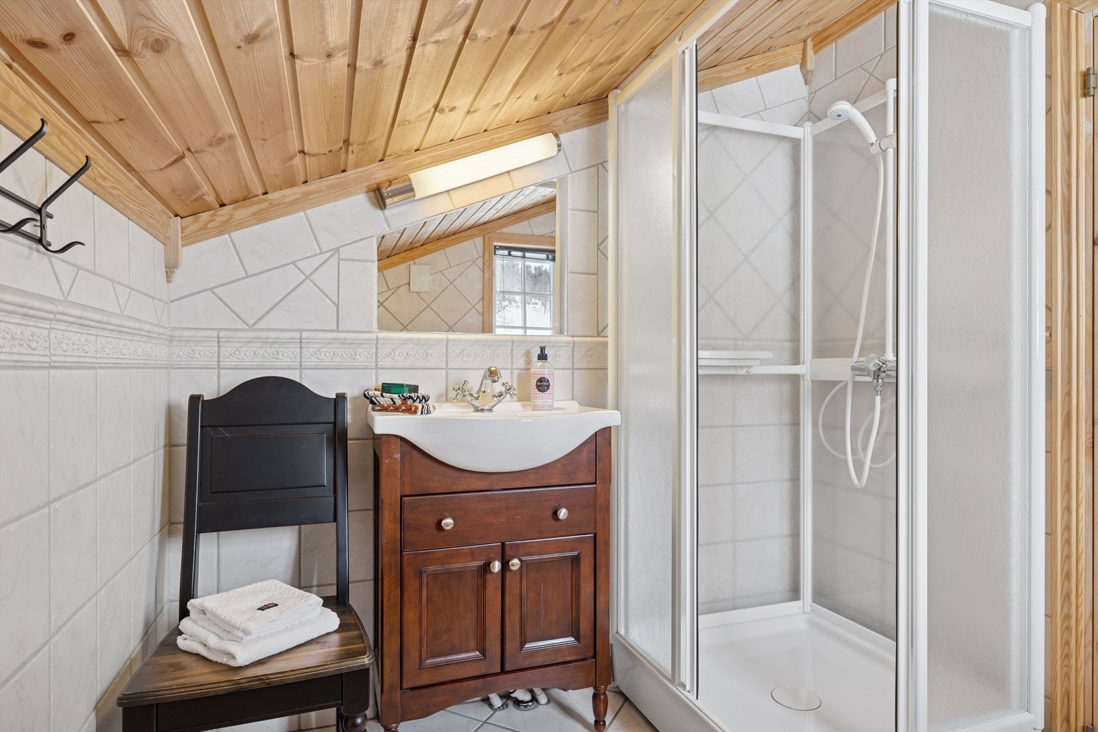 Bad i andre etasje er også stilrent og følger samme design som det første, med fliser på både vegger og gulv. Gulvvarme med varmekabler gir ekstra komfort. Badet er utstyrt med toalett, dusjkabinett og en heldekkende servant med skap under fo Galleribilde