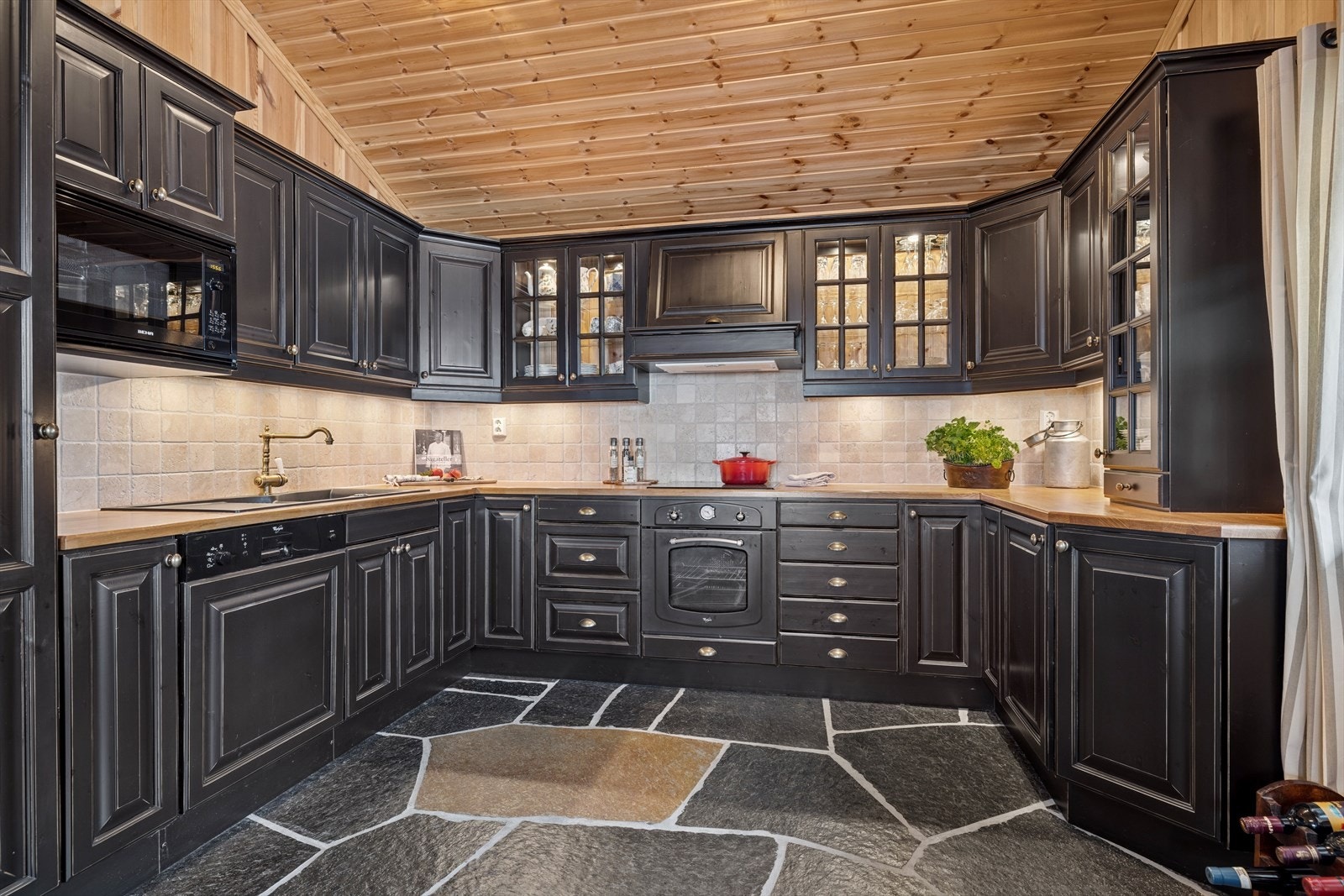 Innredningen har mørkbeisede profilerte fronter, benkeplate i heltre. Av hvitevarer har kjøkkenet integrert steketopp med overhengende ventilator med avtrekk til yttervegg, stekeovn, mikro, oppvaskmaskin og kjøleskap. Galleribilde