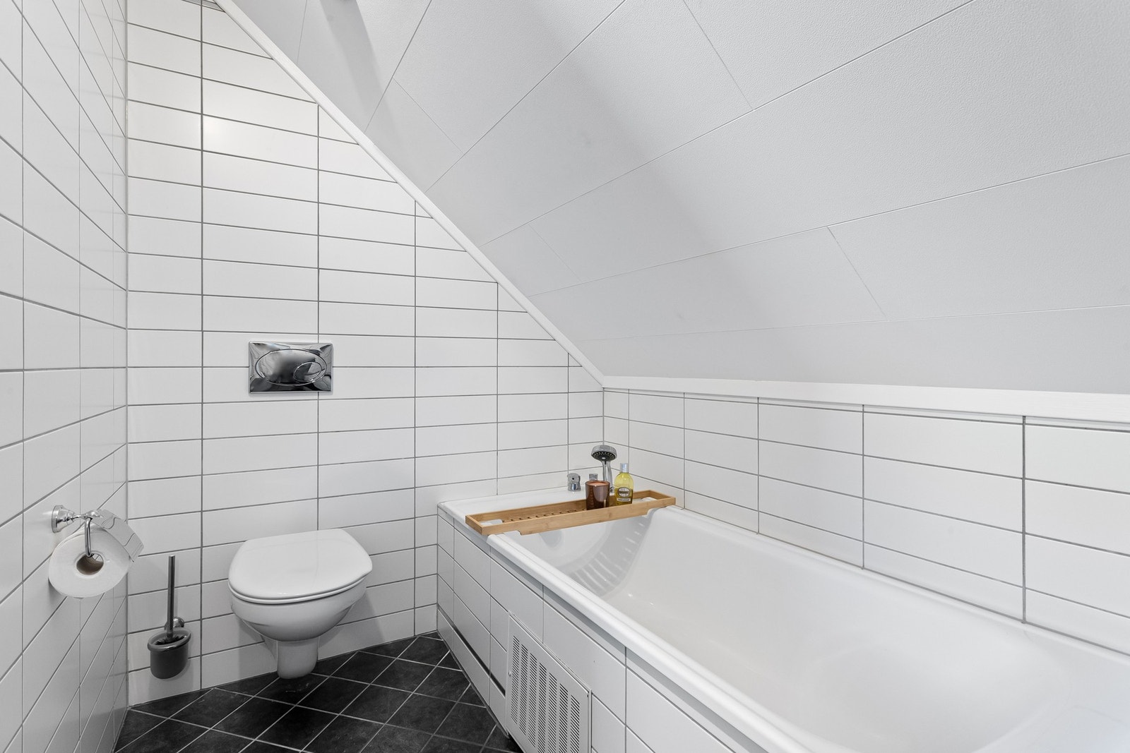 Badet er innredet med innfliset badekar, vegghengt toalett og servant med speil. Galleribilde