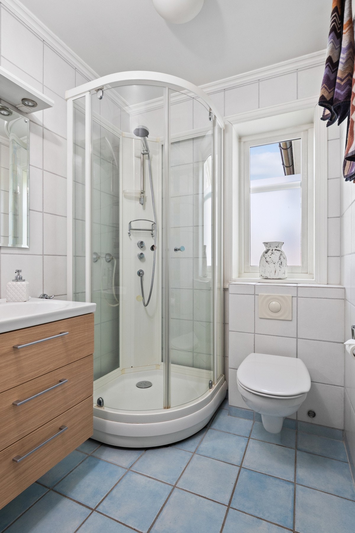 Badet nede er innredet med hvite veggfliser og lyseblå fliser på gulvet. Galleribilde