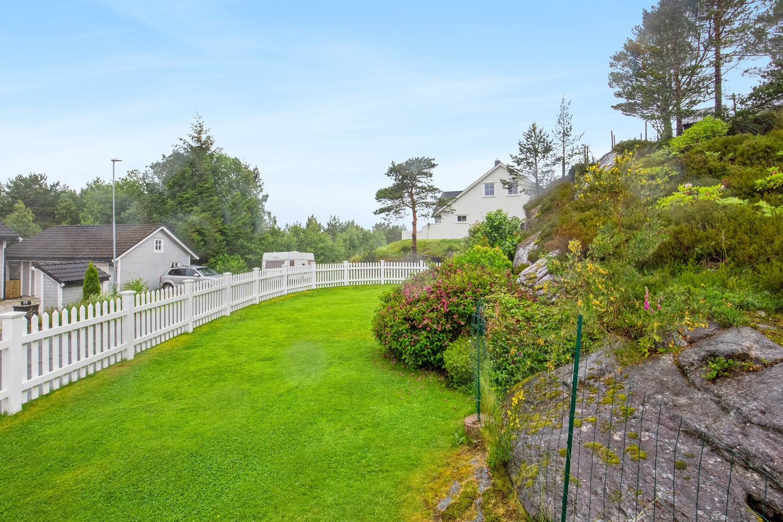 Tomten er opparbeidet med støttemur, plen og stakittgjerde Galleribilde