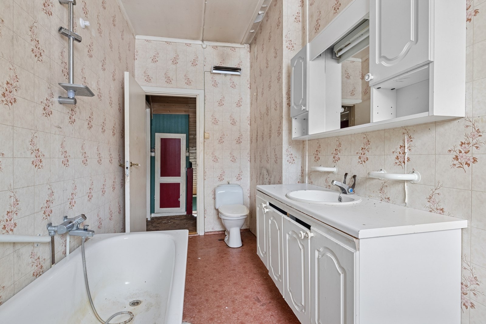 Badet inneholder servantskap med laminat benkeplate og nedfelt servant samt overskap med speil, badekar med dusj og gulvmontert toalett Galleribilde