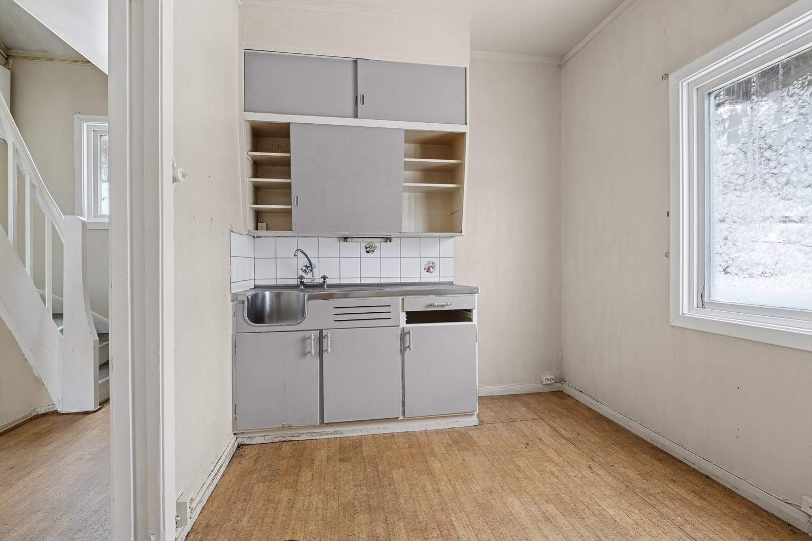 Innredning med malte slette fronter. Laminat benkeplate og heldekkende stålbeslag med oppvaskkum og utslagsvask. Det er fliser over benk. Galleribilde