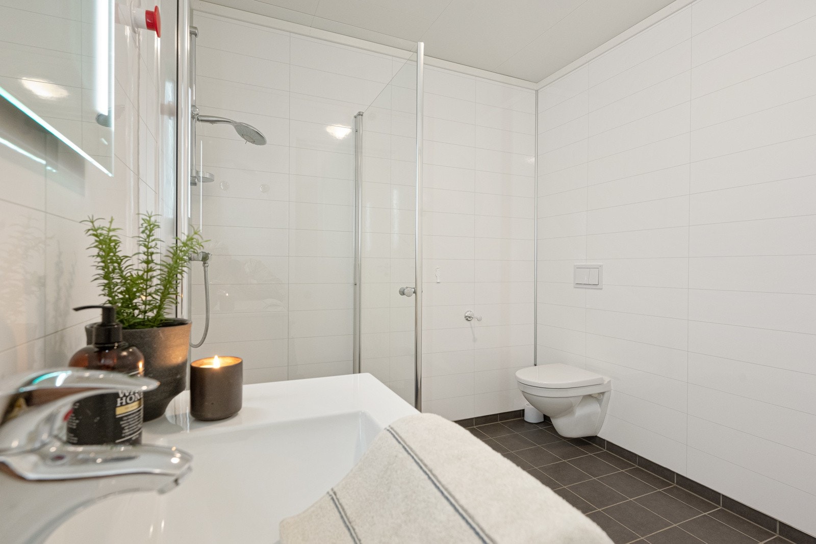 Badet er innredet med baderomsinnredning, vegghengt toalett, dusjdører og opplegg for vaskemaskin. Galleribilde