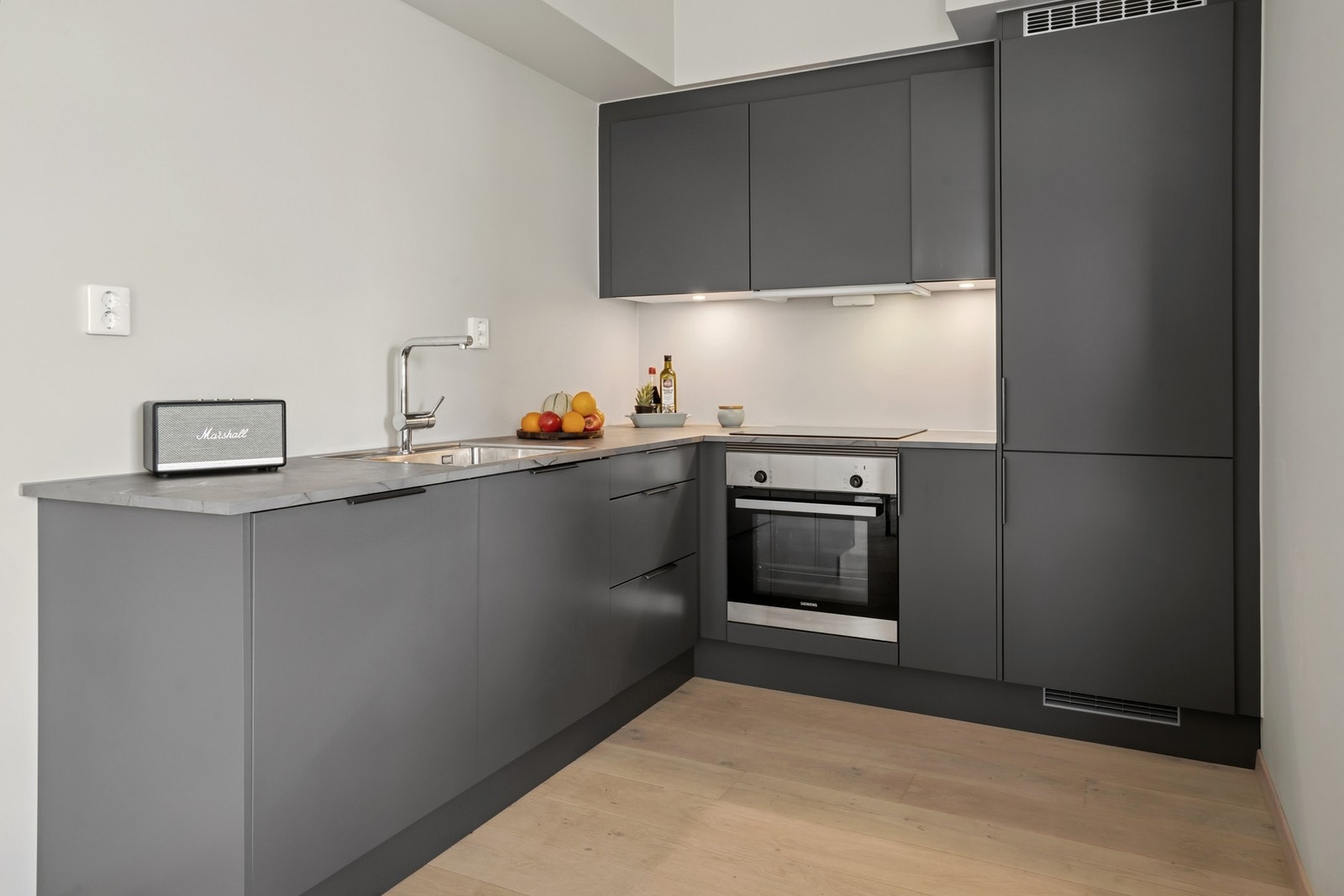Stilrent og moderne kjøkken fra åpen løsning mot stuen. Innredning med grå glatte fronter med foring opp til nedkassinger. Galleribilde