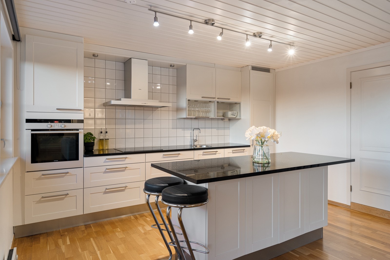 Den tidløse kjøkkeninnredningen fra HTH med hvite, profilerte fronter og sort granittbenkeplate gir rommet et moderne og stilrent preg Galleribilde