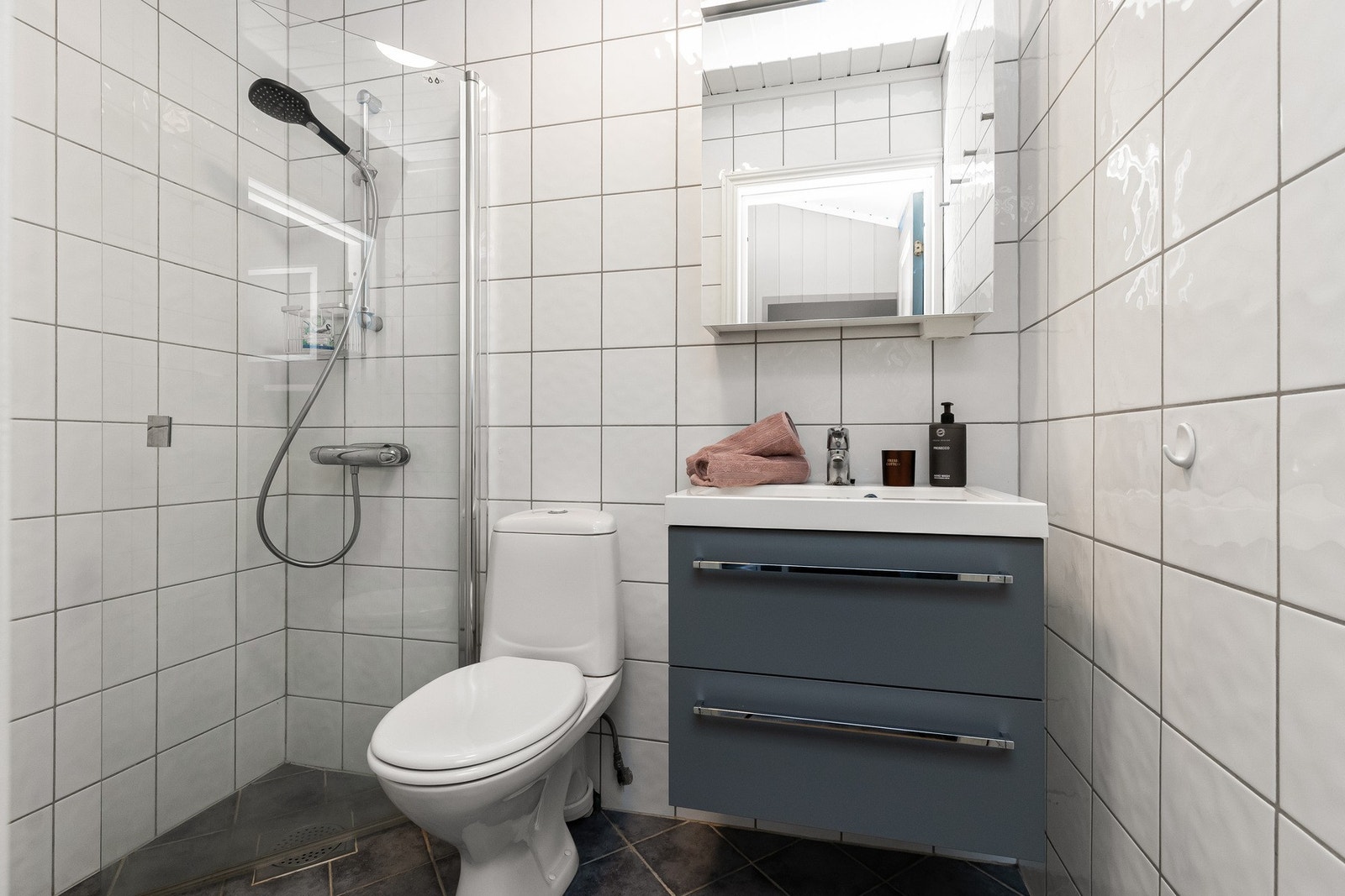 Flislagt bad med mørke fliser på gulv med varmekabler og lyse fliser på vegg. Galleribilde