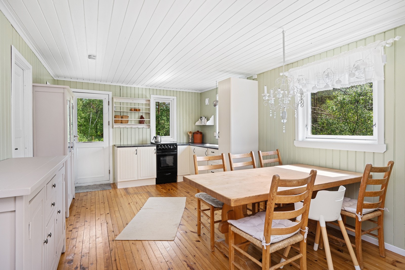 Innredningen har hvitmalte, profilerte fronter, åpne hyller og en mørk laminatbenkeplate med nedfelt oppvaskkum Galleribilde