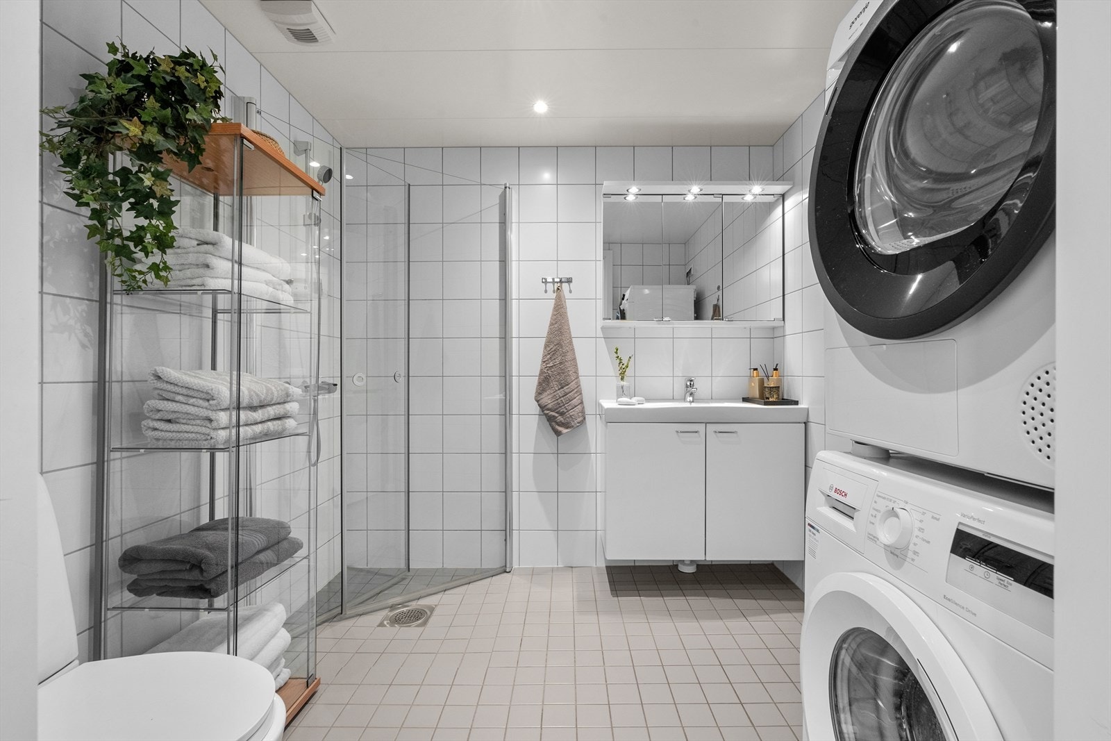 Badet har benkeskap med glatte fronter, servant, dusj på gulv med innfellbare glassdører i herdet glass, opplegg for vaskemaskin og vegghengt klosett. Galleribilde