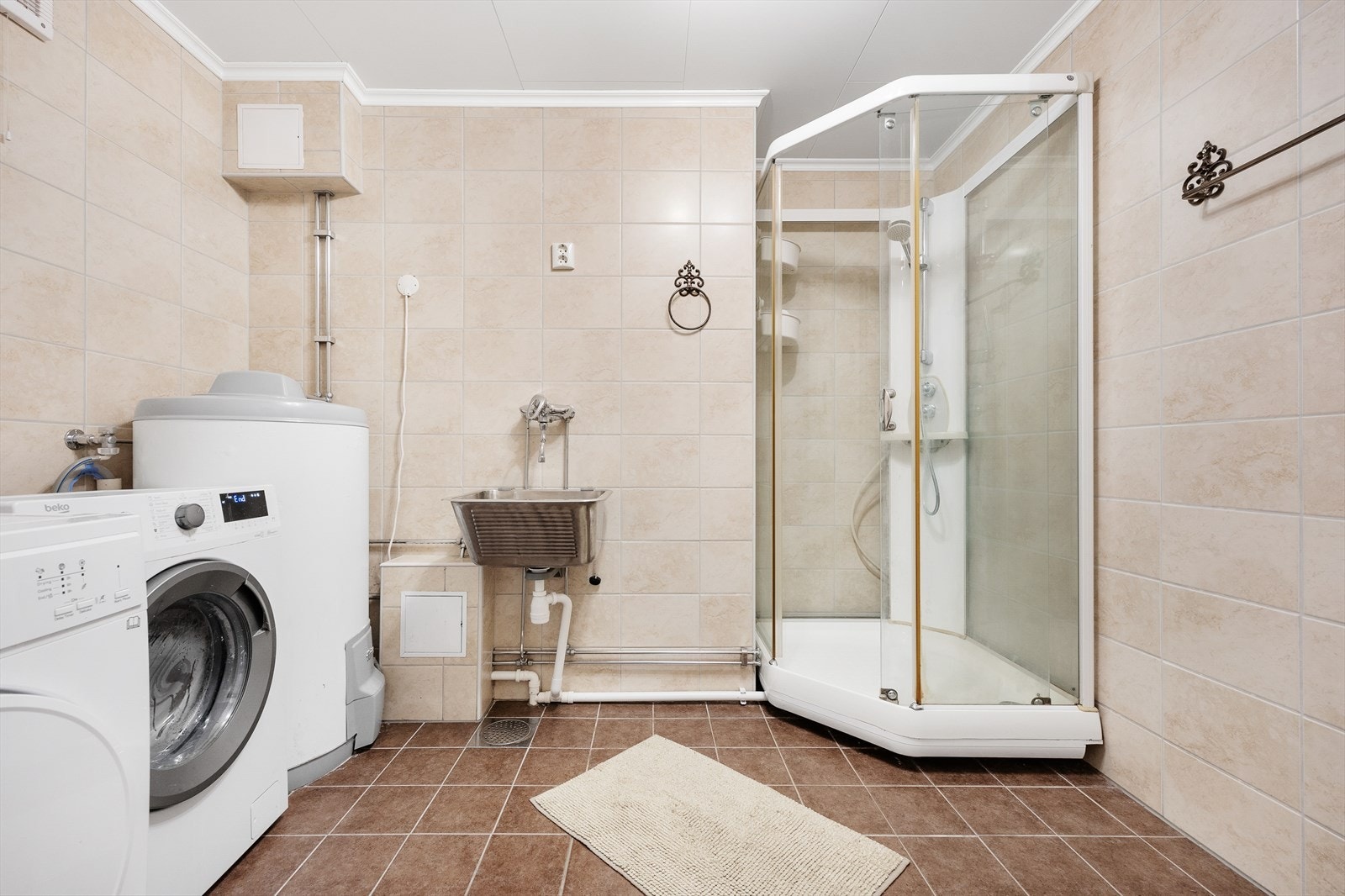 Innredningen består av et underskap, nedfelt servant, speil med belysning over, gulvstående toalett, utslagsvask og et dusjkabinett. Det er opplegg for og plass til vaskemaskin og tørketrommel, samt varmtvannsberederen på ca 200 liter er plassert her Galleribilde