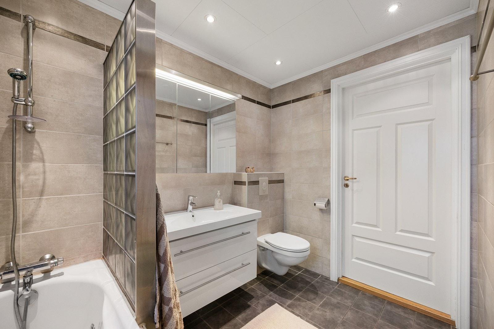 Innredningen består av et underskap, nedfelt servant, speilskap med belysning over og et innebygd badekar med dusjing direkte på vegg. Galleribilde