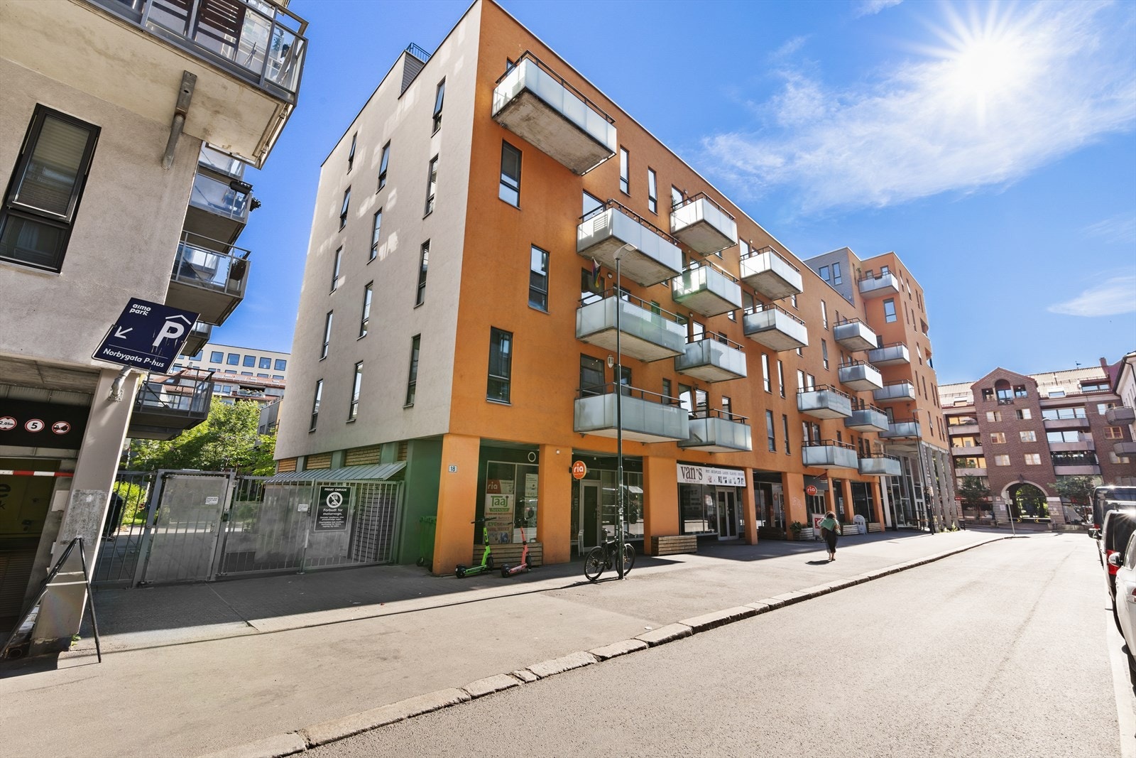 Bygningen har moderne fasade med balkonger og nærhet til koselige kafeer og butikker rett utenfor inngangsdøren. På venstre side av porten ligger et P-hus med mulighet for å leie parkering Galleribilde