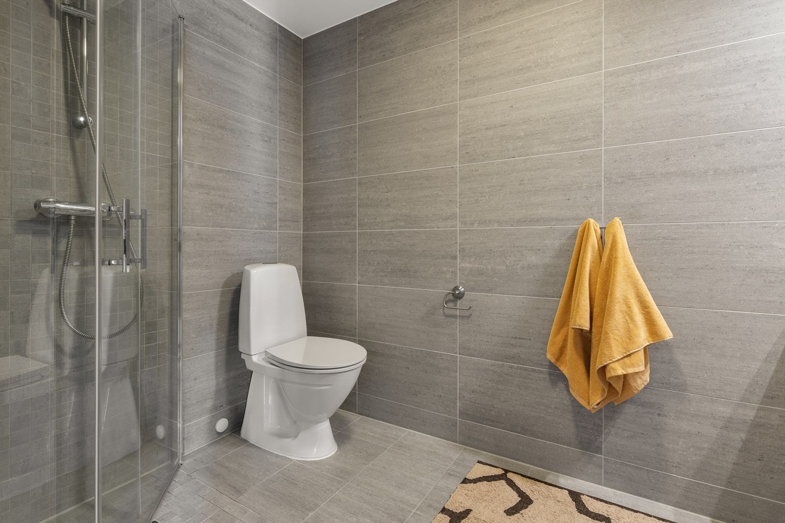 Delikat, flislagt bad med dusjhjørne og vegghengt toalett for enkel rengjøring Galleribilde