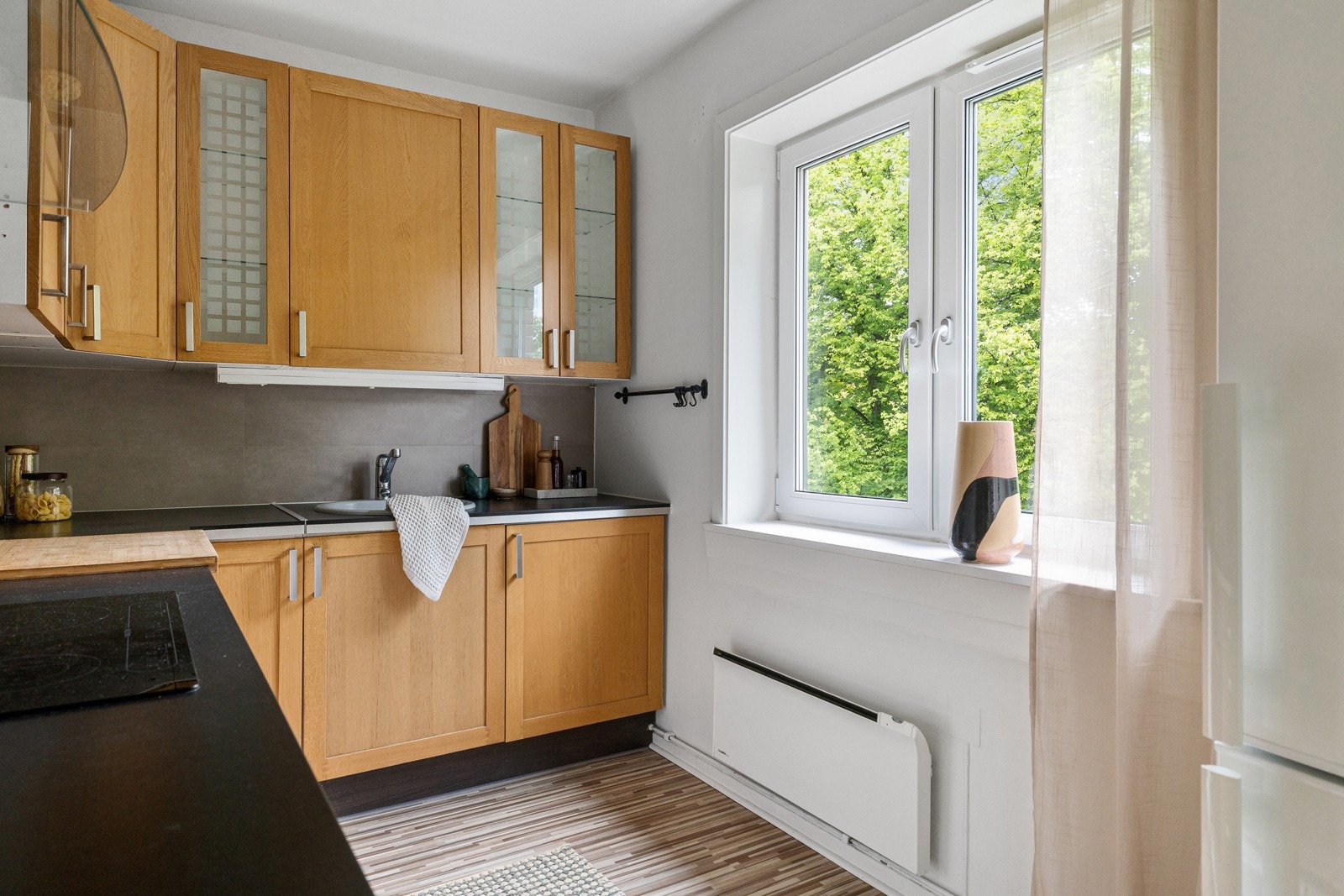 Laminat benkeplate med nedfelt stålkum og keramisk platetopp gir et funksjonelt og elegant uttrykk. Videre er kjøkkenet utstyrt med integrert komfyr, smal oppvaskmaskin samt kombinert kjøl/frys. Galleribilde