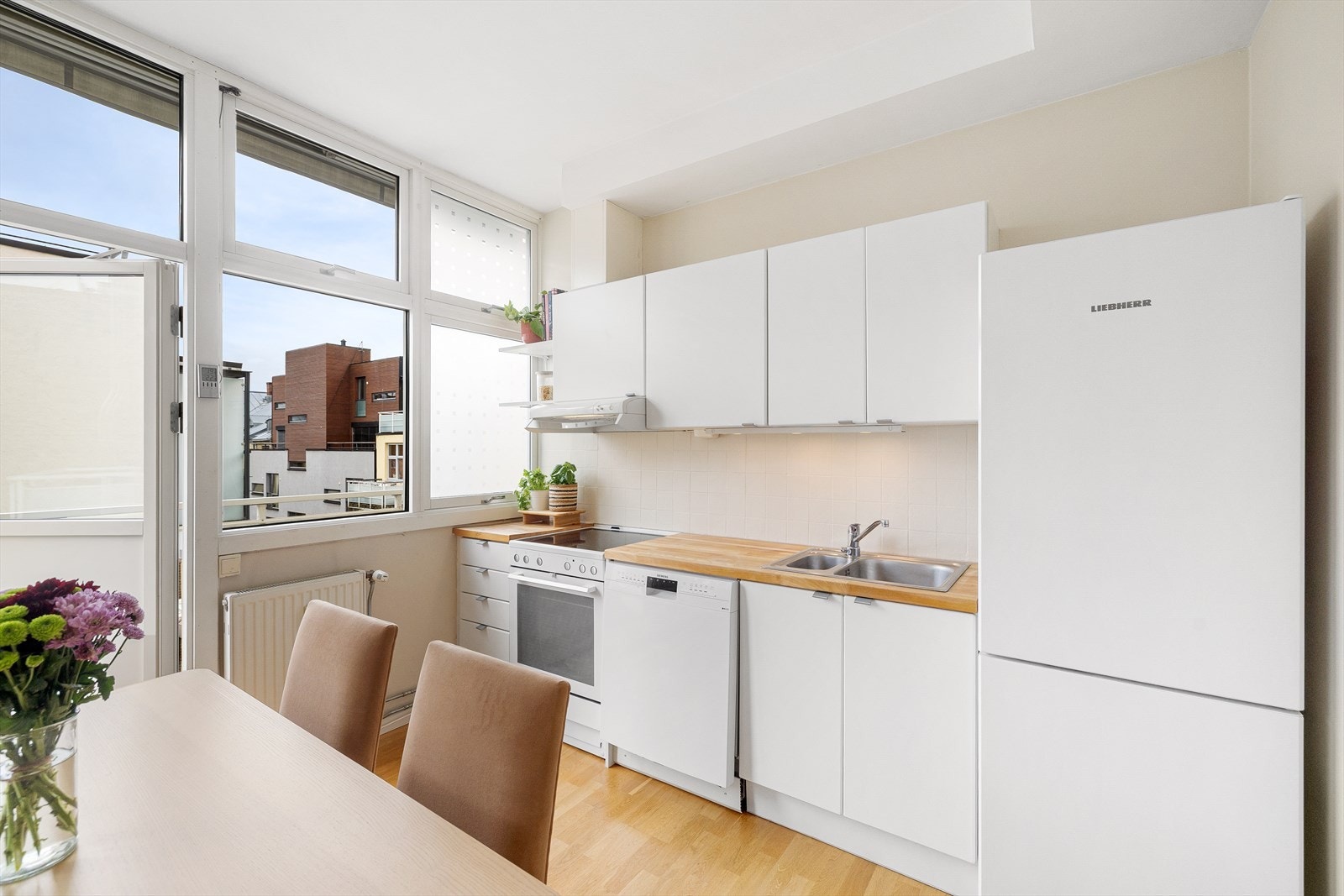 Innredning med hvite glatte fronter, benkeplate i tre og flislagt på veggen over kjøkkenbenken. Galleribilde