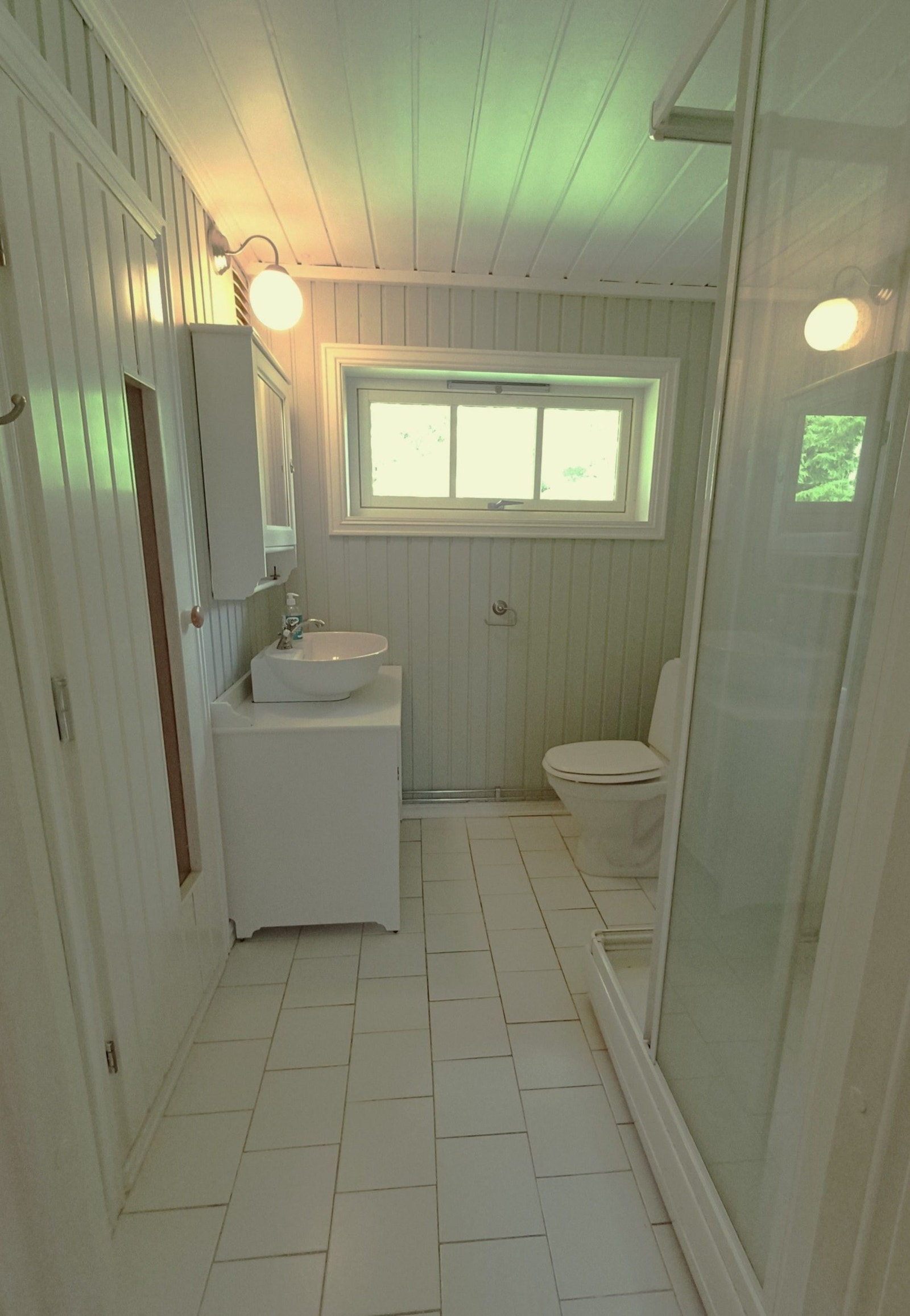 Bad med flislagt gulv og varmekabler. Malte vegger og utstyrt med toalett, servant på skap og dusjkabinett. Galleribilde