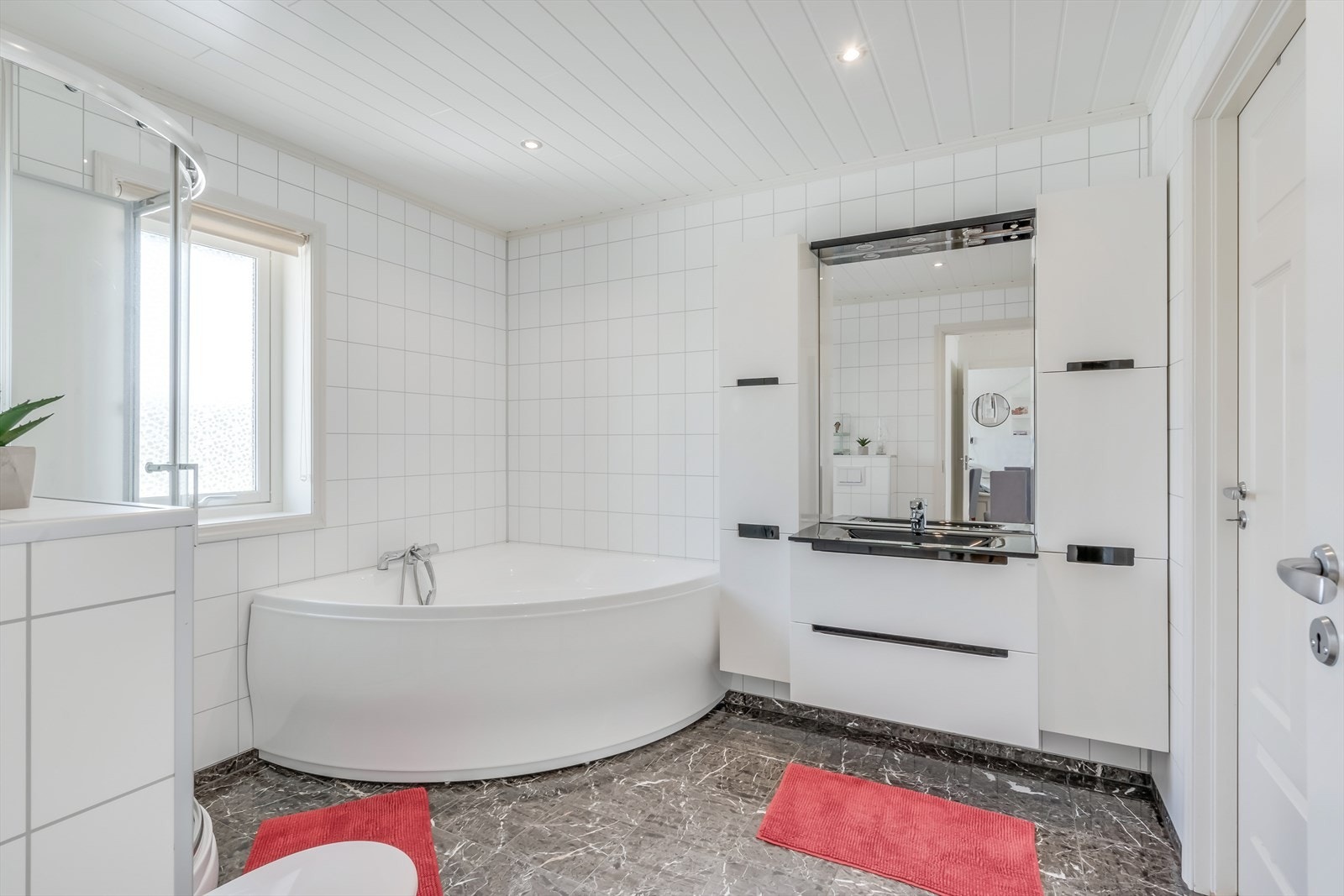 Lyst og pent bad med badekar, dusjkabinett, vegghengt toalett og innredning. Galleribilde