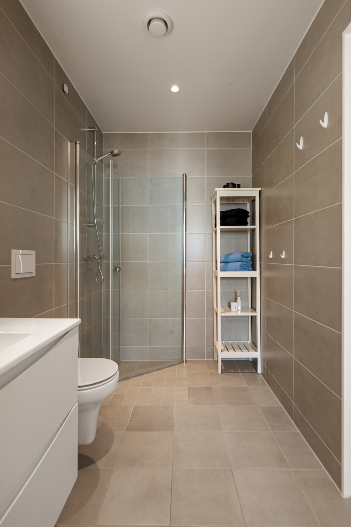 Det er lagt beige fliser på både gulv og vegger. Badet er utstyrt med baderomsinnredning, veggmontert wc, dusjhjørne med innfellbare dører og speil med integrert belysning Galleribilde