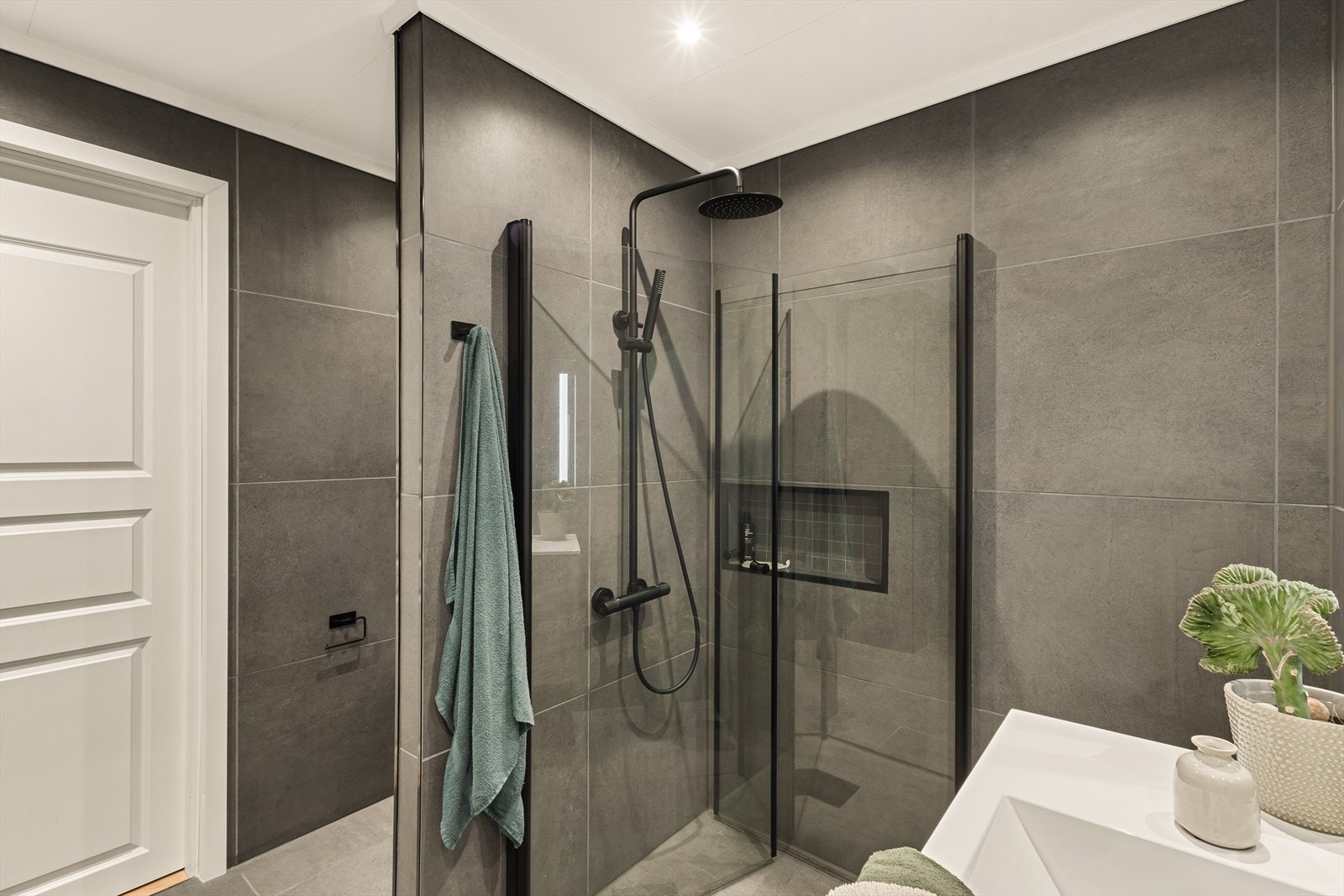 Et rålekkert bad med regndusj, sorte detaljer og innfelt hylle i dusjen. Galleribilde