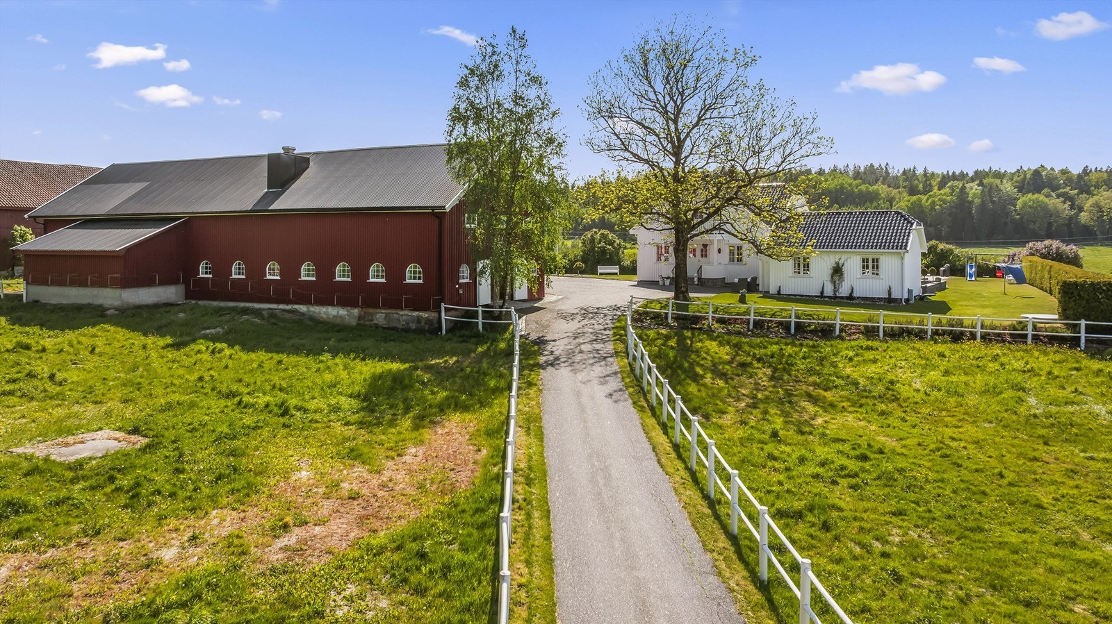 Man kjører inn fra Åsrumveien og inn på egen eiendom. Asfaltert vei inn med PVC-hestegjerder på hver side av veien. Galleribilde