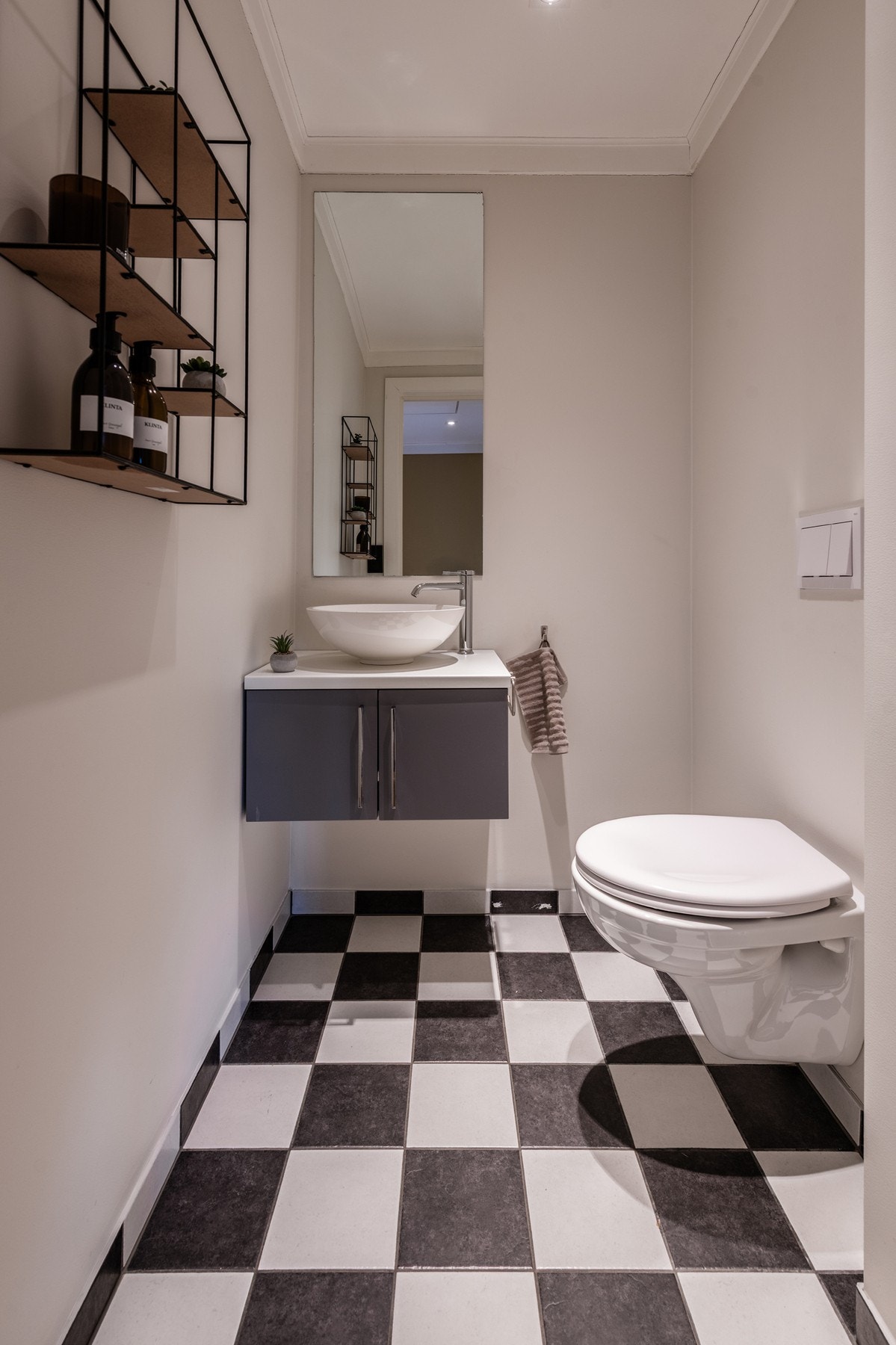 Et stilrent, praktisk og flislagt toalettrom innredet med vegghengt toalett med innebygd sisterne og servant med underskap. Galleribilde