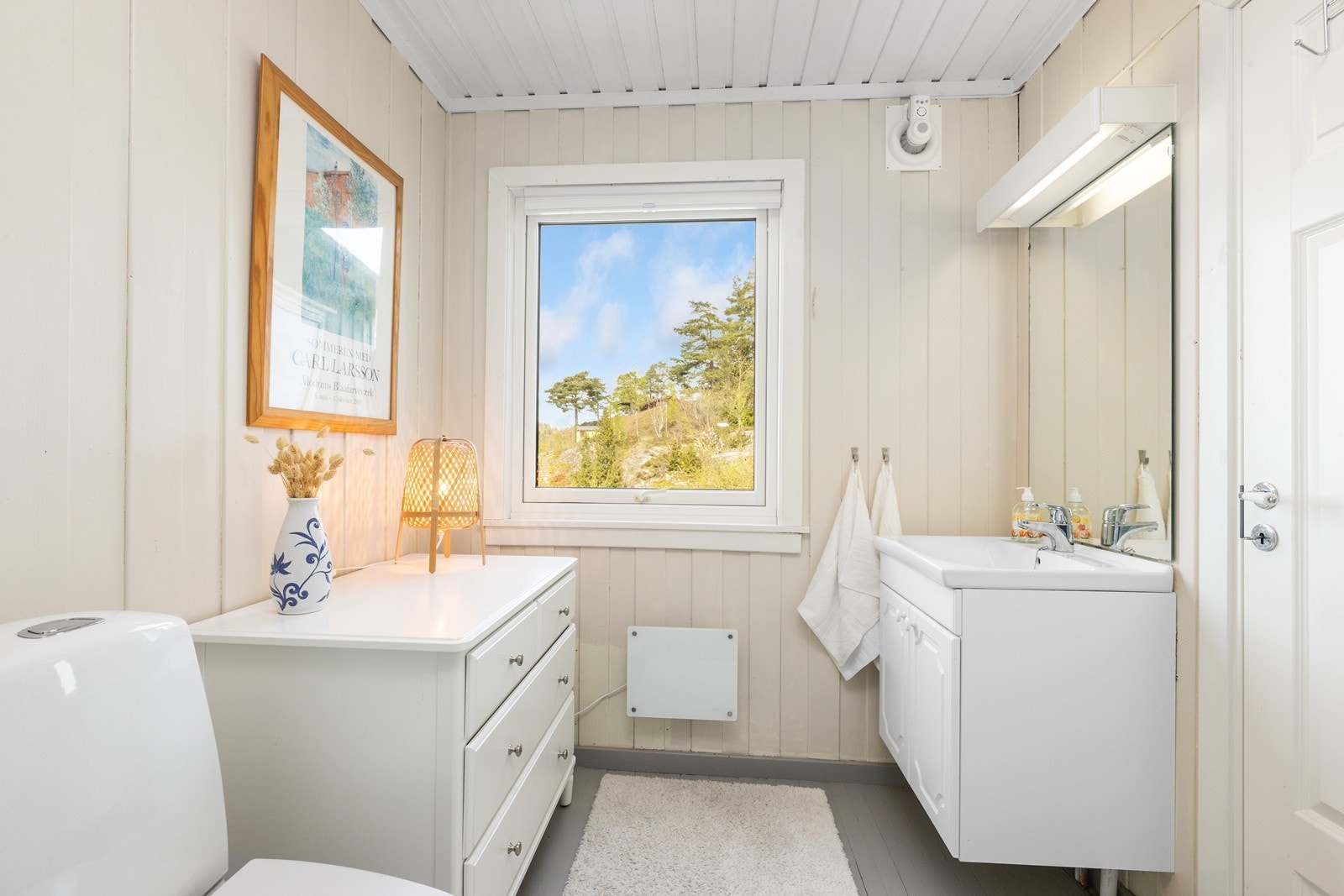Lyst og pent bad med malte treoverflater. Badet er innredet med servantskap, servant, speil, dusjkabinett og toalett. Galleribilde
