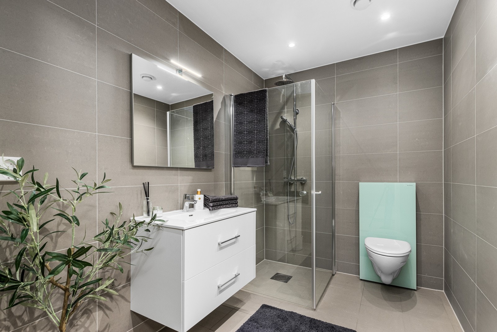 Flislagt bad med servantskap, dusjhjørne og Monolith vegghengt toalett. Galleribilde