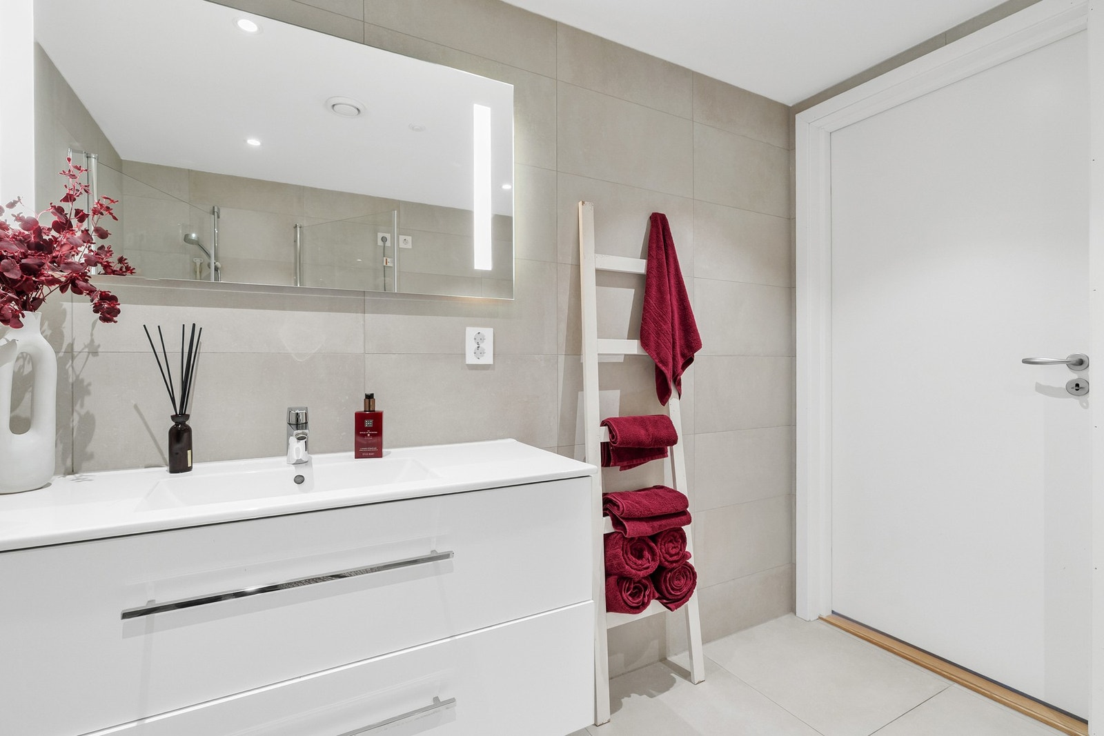 Rommet er innredet med hvit servantinnredning, speil med integrert belysning, gulvstående toalett, dusjhjørne med innfellbare glassdører samt opplegg for vaskemaskin Galleribilde