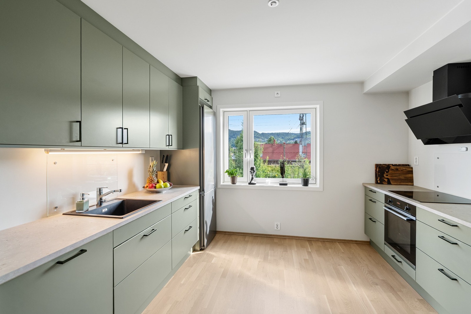 Pen kjøkkeninnredning med slette, lysegrønne fronter og laminat benkeplate med nedfelt sort komposittvask med ettgreps blandebatteri Galleribilde