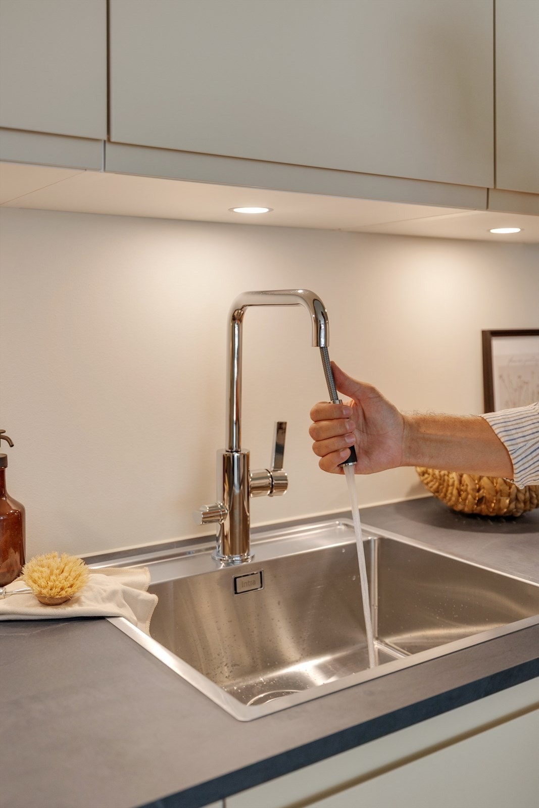 Lekre detaljer på kjøkken som innfelte LED spotter i overskap med dimmer montert på vegg, slimline kjøkkenventilator fra Røros, integrerte hvitevarer, kjøkkenkran med uttrekk, automatisk vannstopper og komfyrvakt Galleribilde