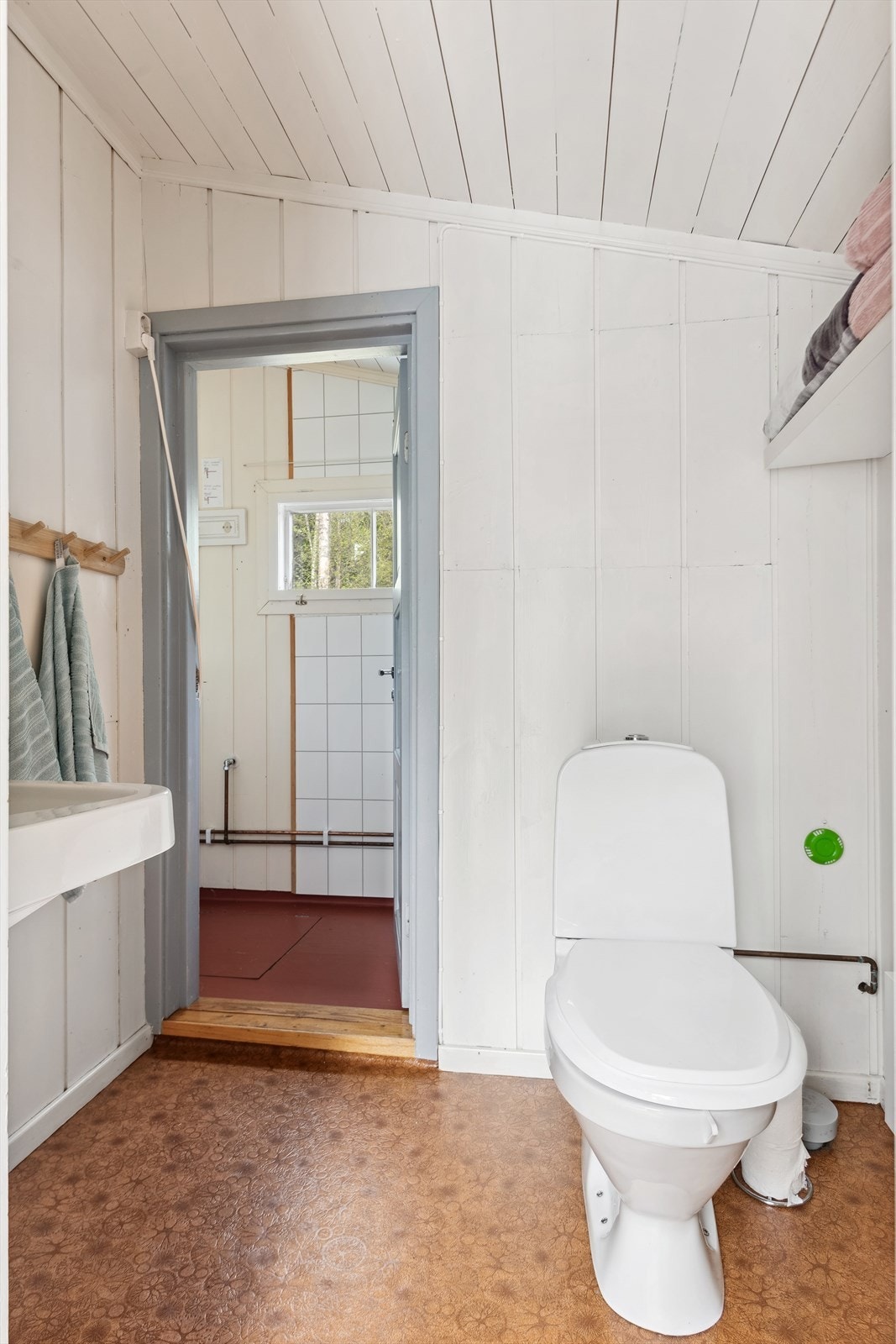 Baderommet har vinylbelegg på gulvet og malt panel på veggene, og baderomsplater i dusjsonen. Første delen av badet er innredet med servant montert på vegg, vegghengt skap med speil og toalett. En dør skiller inn til neste del av badet. Galleribilde