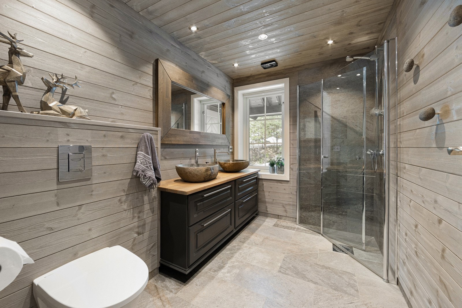 Nydelig bad som har innredning med benk med to vasker og speil, flislagt dusjsone med vegghengt dusj m/glassdører og vegghengt toalett. Galleribilde