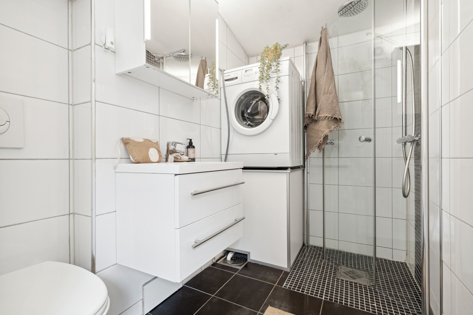 Funksjonelt baderom utstyrt med toalett, servant, dusjhjørne med innfellbare glassdører og tropedusj, samt opplegg for vaskemaskin. Galleribilde