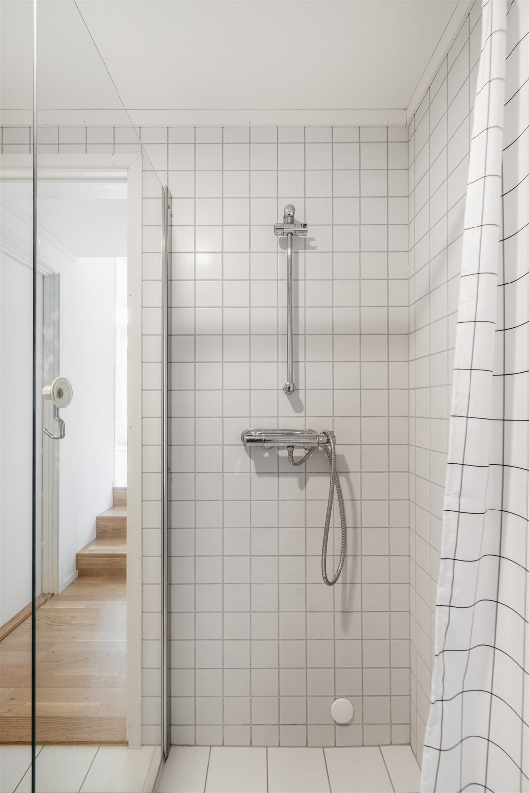 Badet er utstyrt med veggmontert toalett, glassvegg mot dusjnisje samt dusjgarnityr og elektrisk styrt vifte. Galleribilde