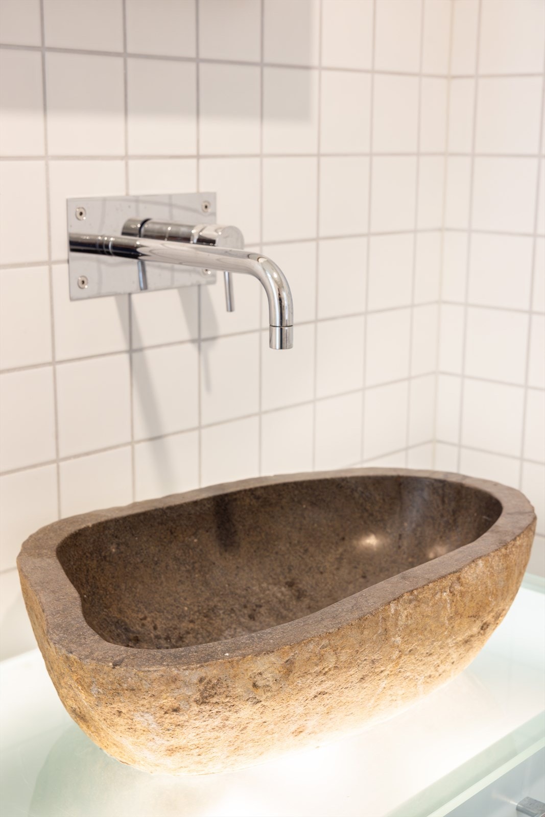 Innredningen har benkeplate av glass med frittstående vask. Over innredningen er det veggmontert blandebatteri. Galleribilde