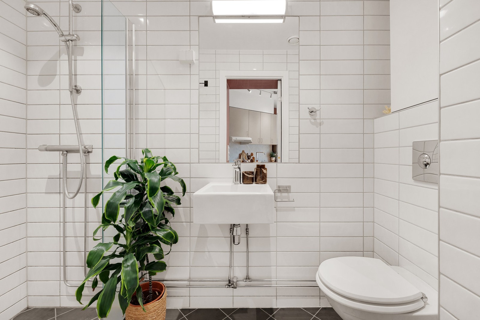 Pent flislagt bad med vegghengt toalett, servant, speil og dusj. Galleribilde