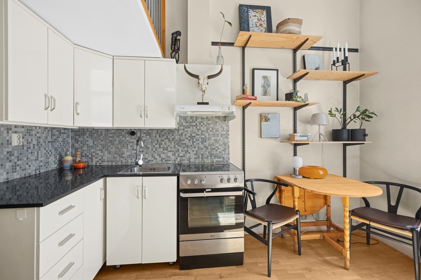 Kjøkkeninnredning består av glatte høyglans skapfronter, benkeplate i stein med fliser på bakvegg og enkel oppvaskkum. Galleribilde