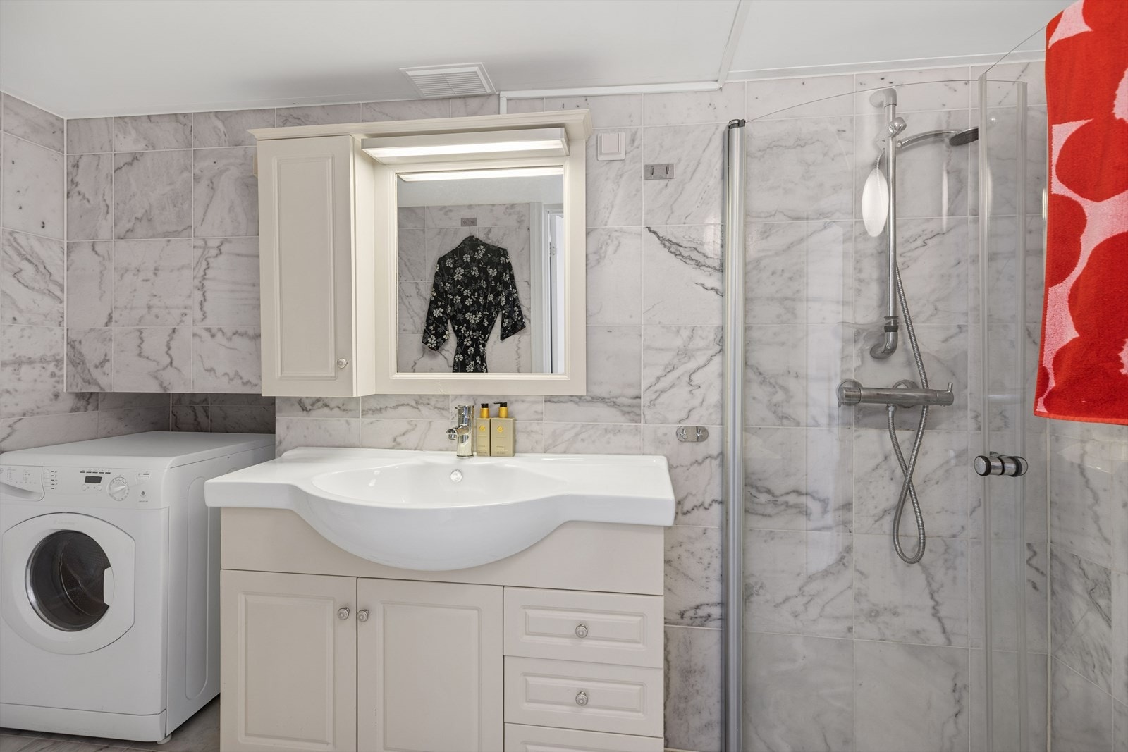 Baderomsinnredning består av servant med underskap, speil med overlys, dusjhjørne med svingbare glassdører, klosett og opplegg for vaskemaskin. Det er mekanisk avtrekk fra baderommet. Galleribilde