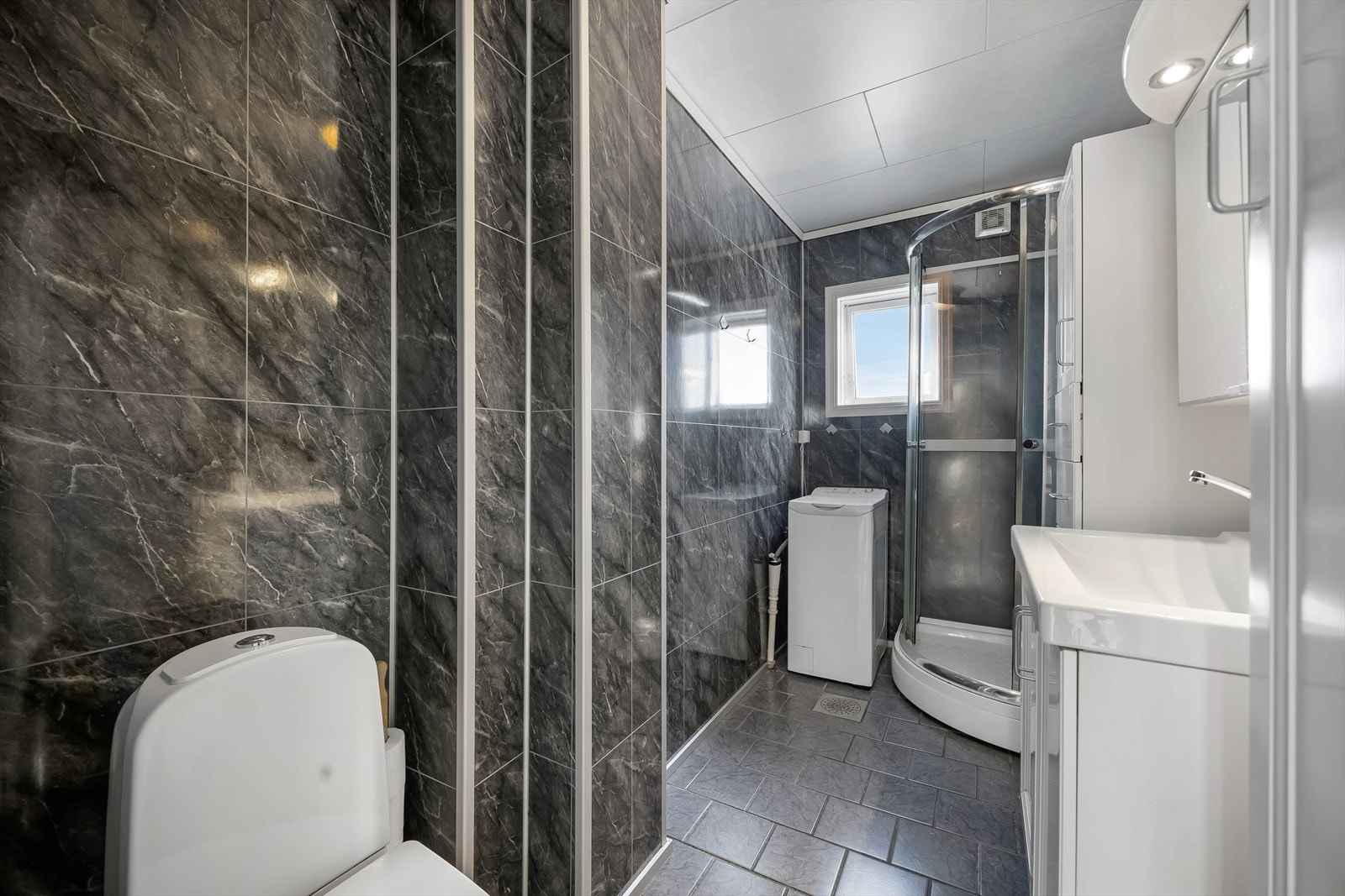 Bad i 1. etasje. Innredet med baderomsplater på vegg og fliselagt gulv. Opplegg til vaskemaskin. Galleribilde