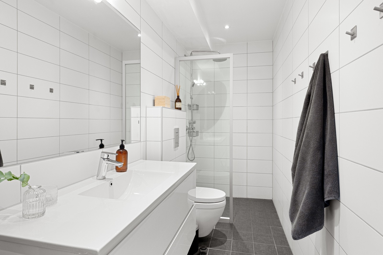 Badet i første etasje er lyst og pent med vannbåren gulvvarme, regnfallsdusj, flislagte overflater og fin innredning. Galleribilde