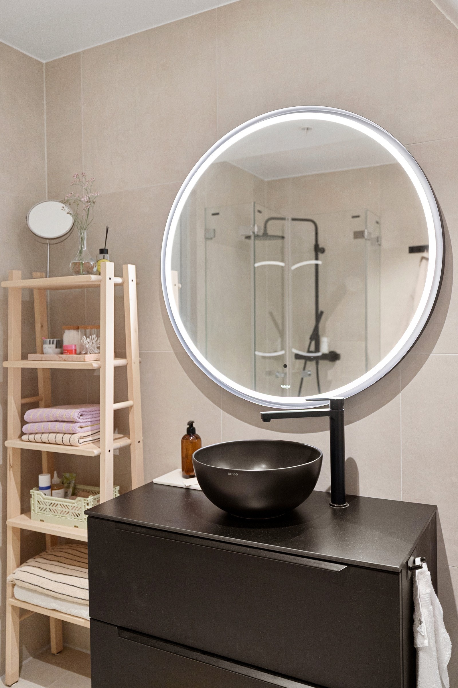 Moderne baderomsinnredning med skuffer og benkeplate med ovenpåliggende bolleservant, stort rundt speil med integrert belysning over. Galleribilde