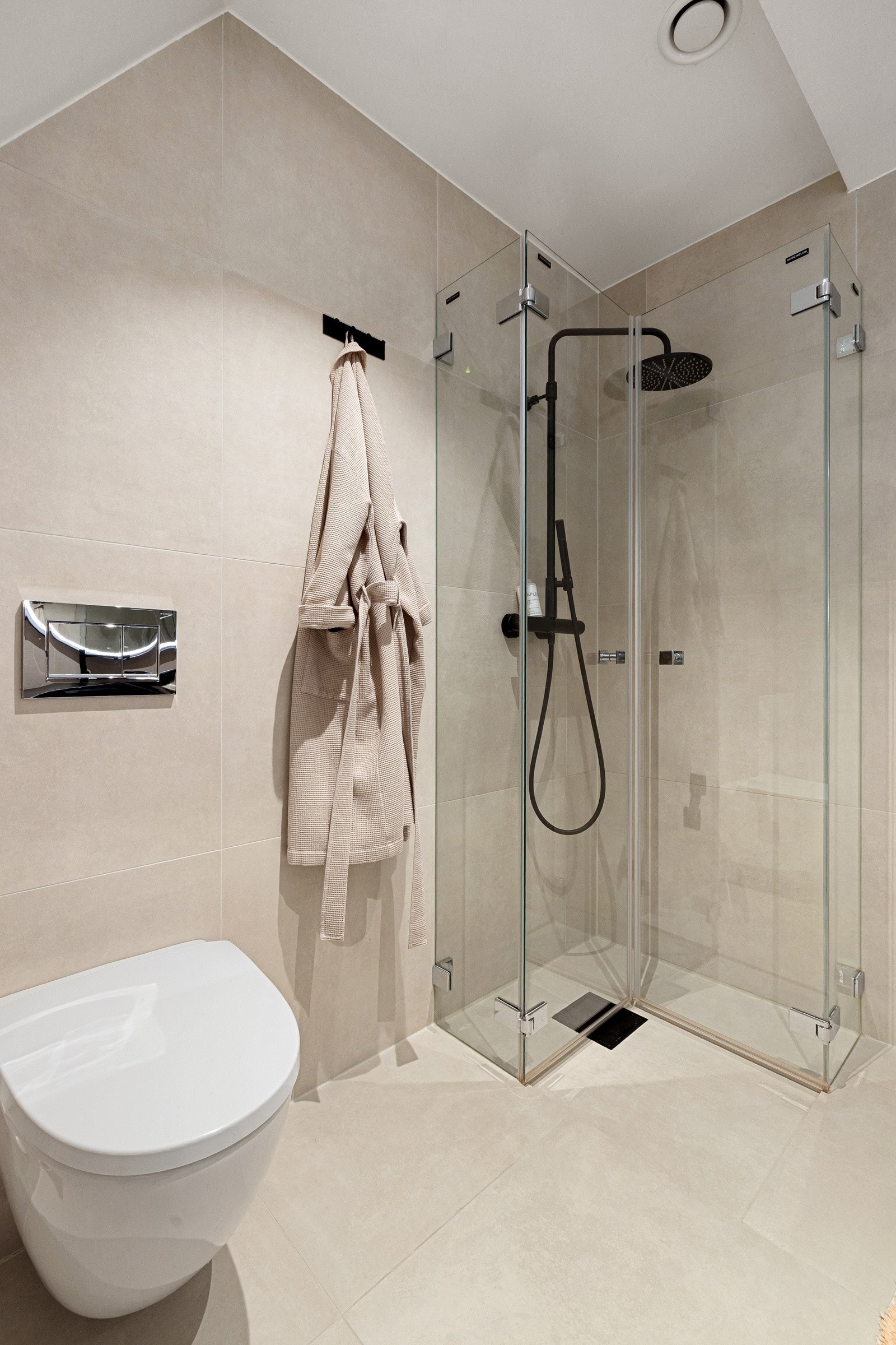 Baderommet er også utstyrt med dusjhjørne med innfellbare glassdører og sort armatur med både hånd- og regnfallsdusj, samt vegghengt toalett. Galleribilde
