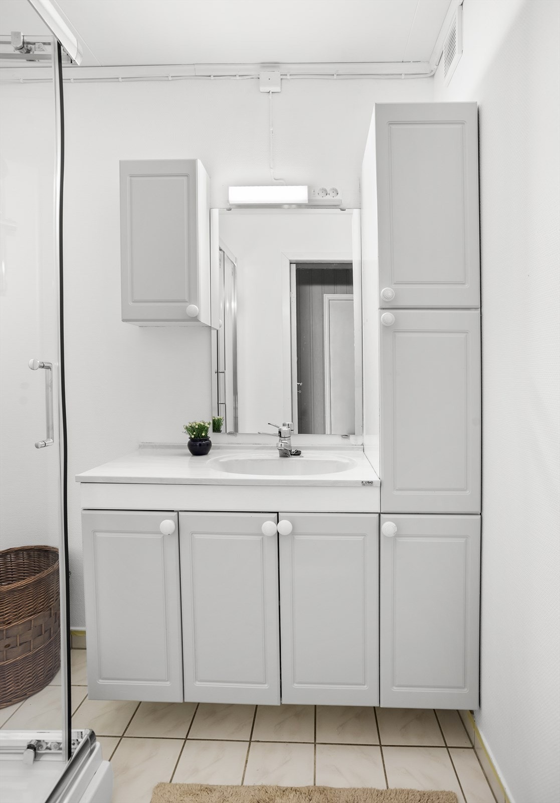 Baderom med vegghengt servant med tilhørende skap, samt dusjkabinett. Galleribilde