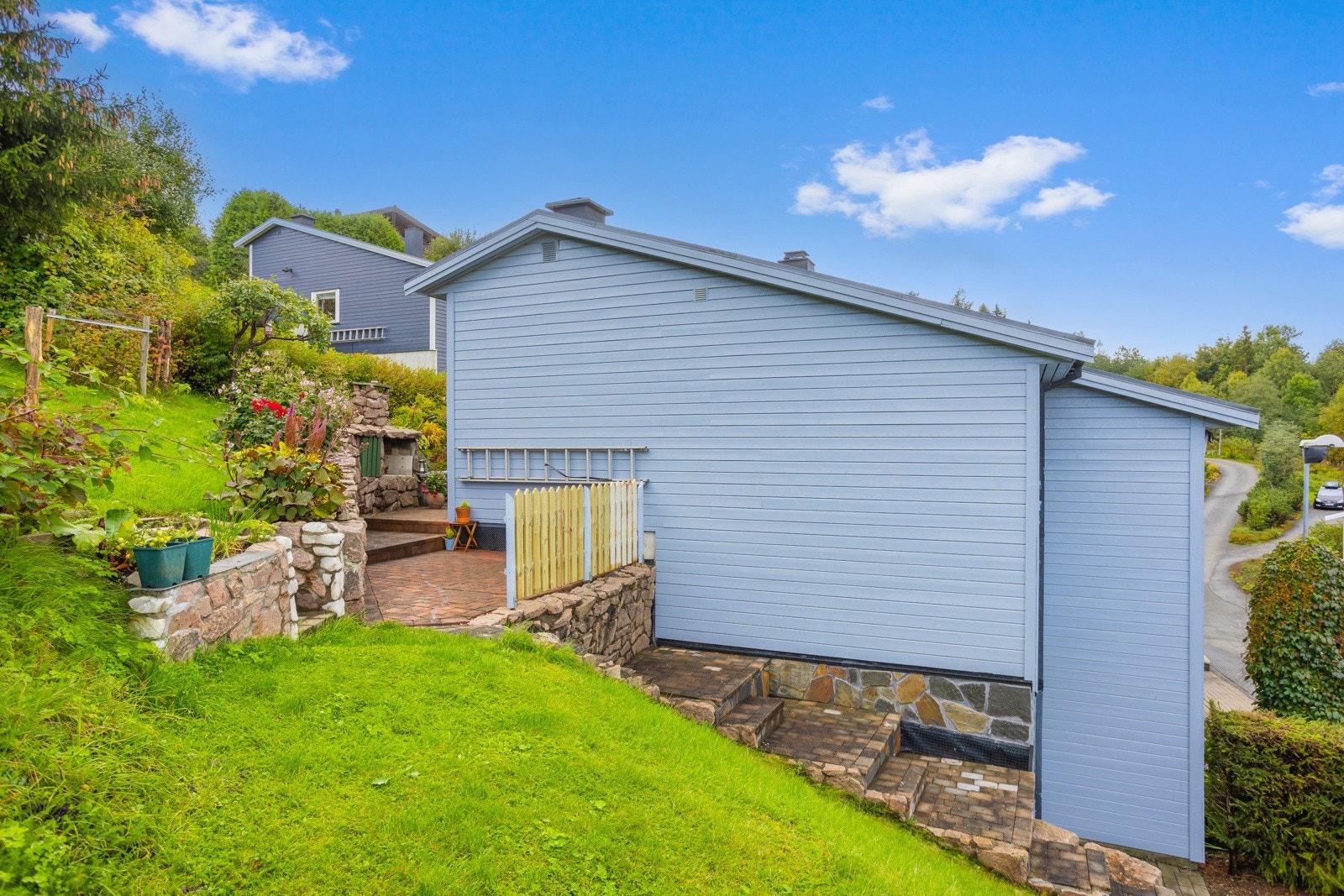 Hage med rips, solbær, bringebær, epletrær og markjordbær. Det er plener og småtrapper rundt hele huset som viltre småbarn kan boltre seg i. Galleribilde