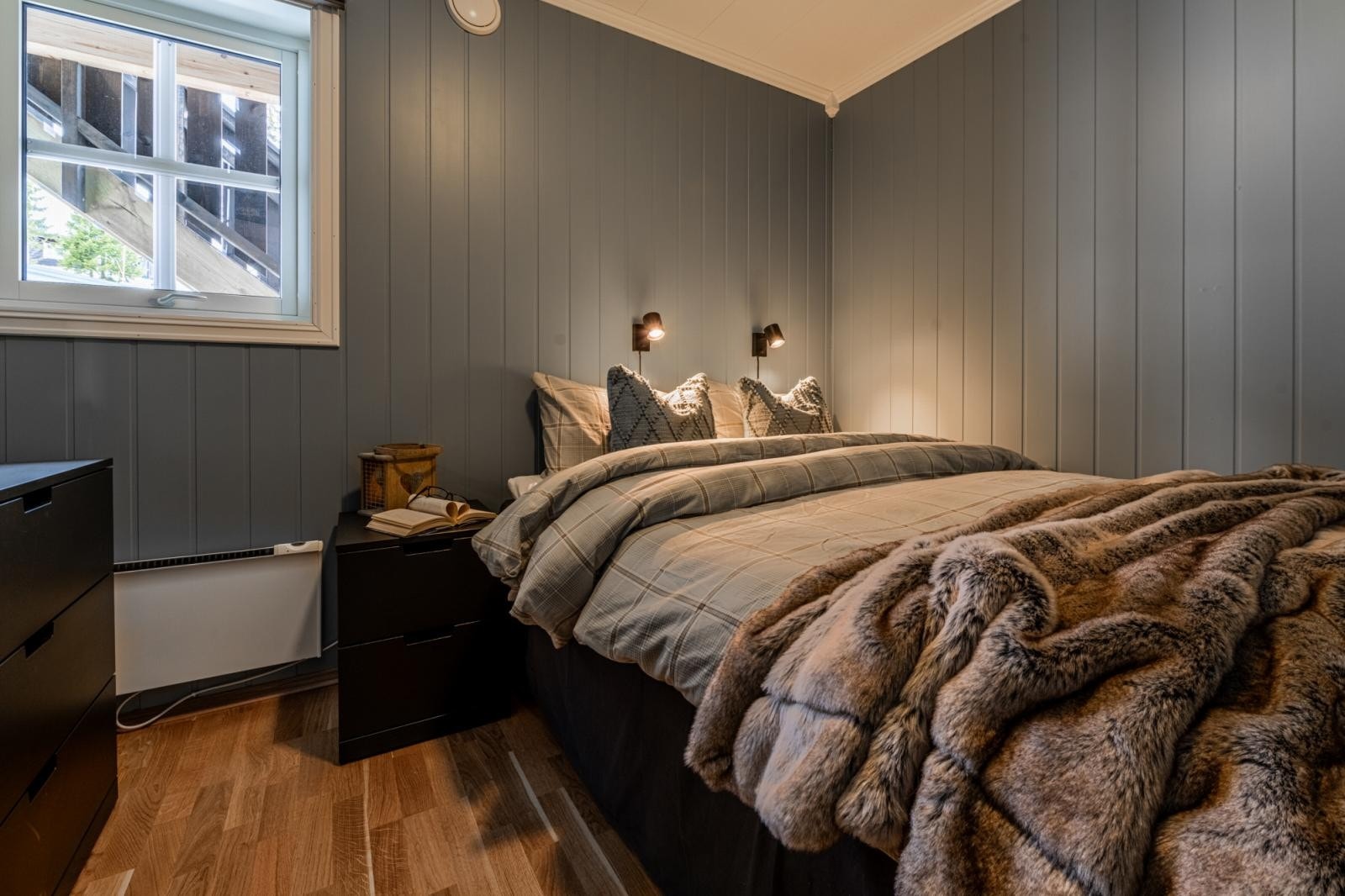 Hovedsoverommet har en stor dobbeltseng. Veggene er malt i en dempet blågrå farge som skaper en lun stemning. To nattbord med vegghengte lamper gir et stilrent uttrykk Galleribilde