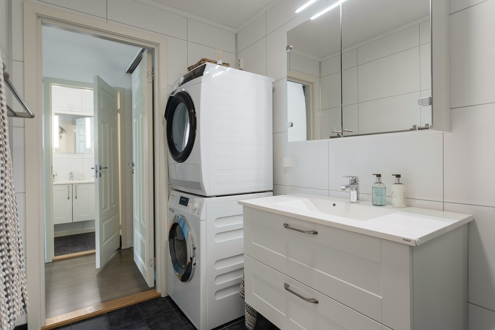 Badet har plass til vaskemaskin og tørketrommel og godt med oppbevaring under servant og i speil. Galleribilde
