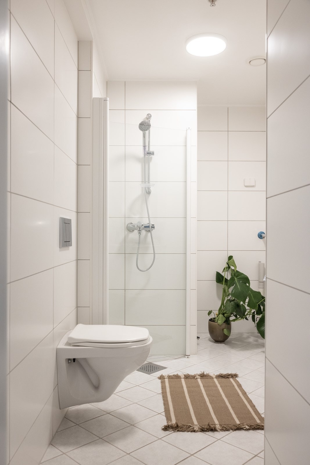 Badet er innredet med vegghengt toalett, dusjhjørne med innfellbare glassdører og baderomsinnredning med skap, servant og speilskap. Galleribilde