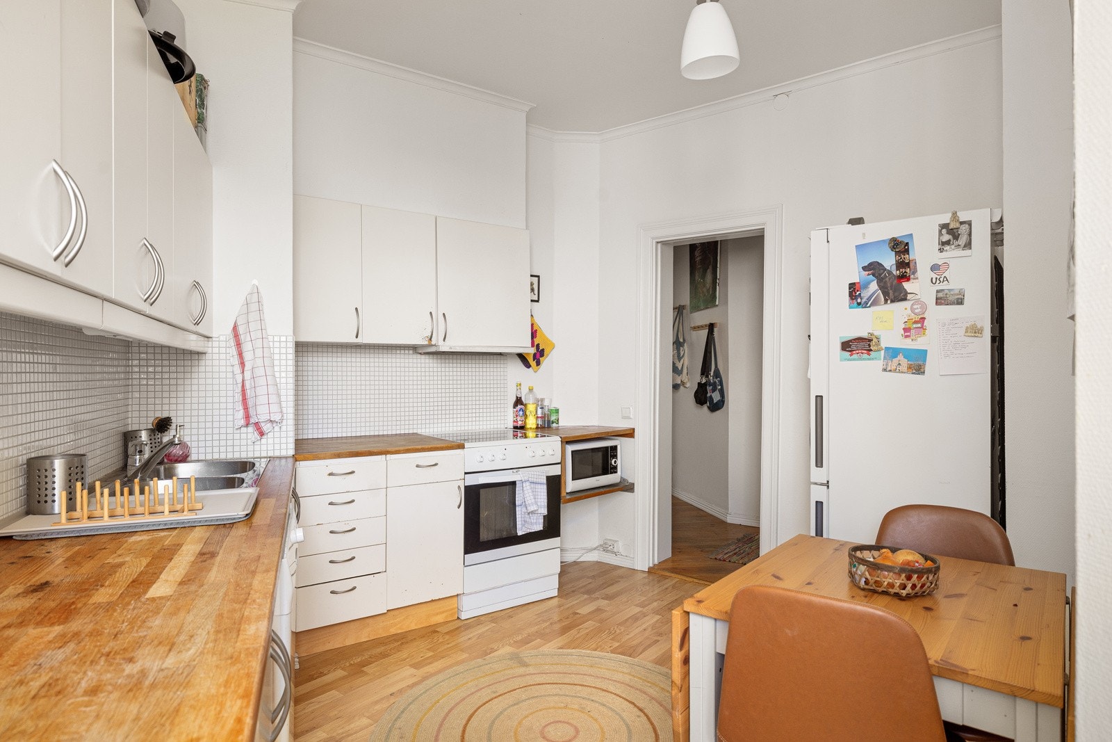 Lys kjøkkeninnredning med god skap- og benkeplass. Innredningen har hvite glatte fronter og heltre benkeplate med nedfelt oppvaskkum. Praktisk med lyse mosaikkfliser i benkeryggen og belysning under overskapene. Galleribilde