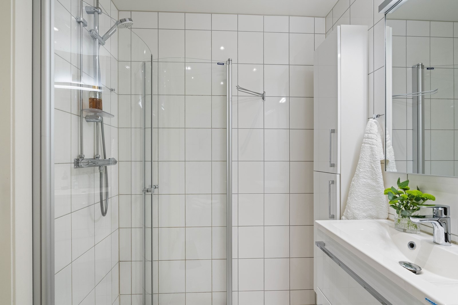 Innredningen består av veggmontert toalett, servant med underskap, speil med integrert belysning og et praktisk høyskap for oppbevaring. Det er også installert dusjløsning med innfellbare glassdører. Galleribilde