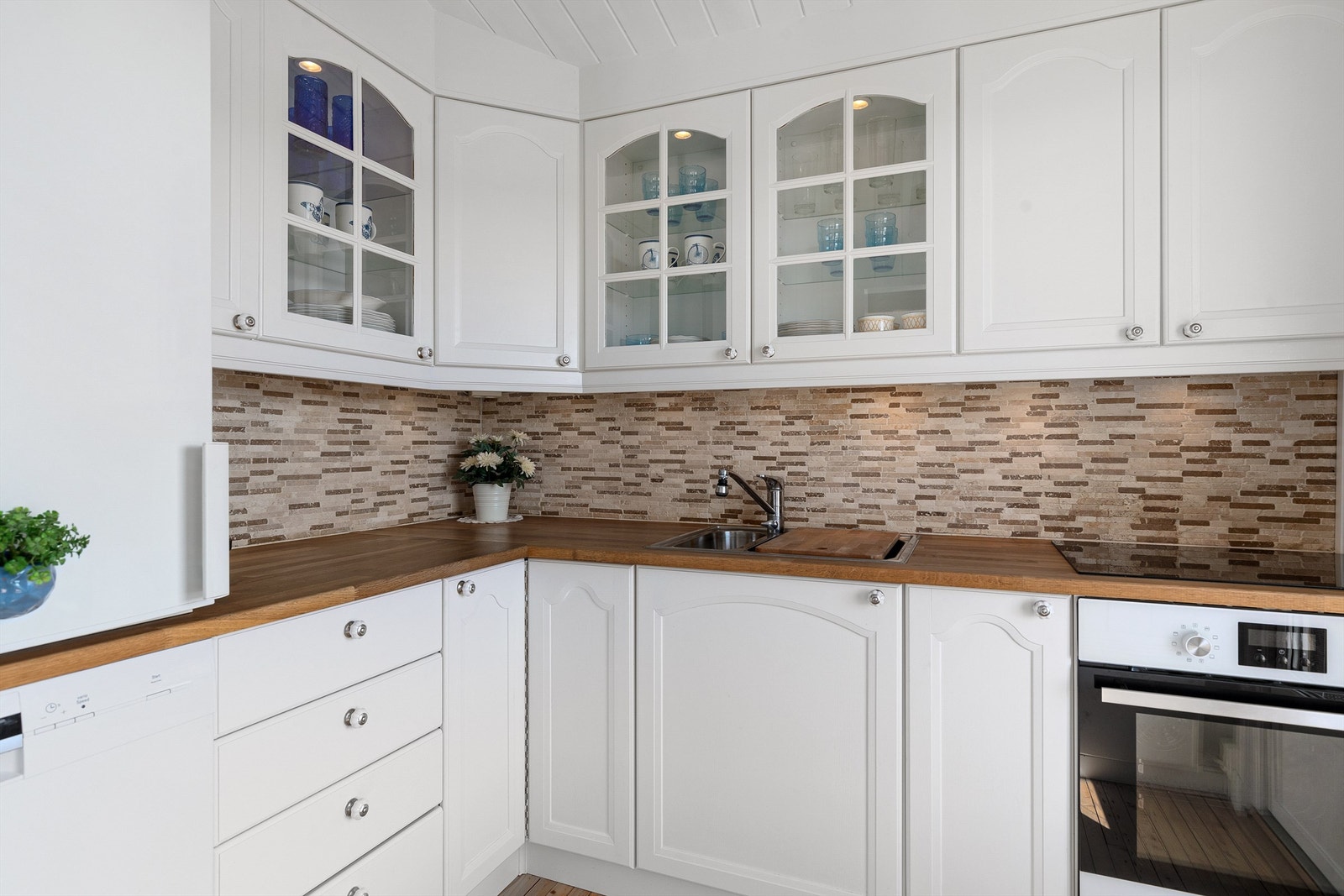 Lyst og pent kjøkken med lyse profilerte fronter. Hvitevarer som oppvaskmaskin, kombiskap, kjøleskap og en komfyr med
separate platetopp medfølger Galleribilde